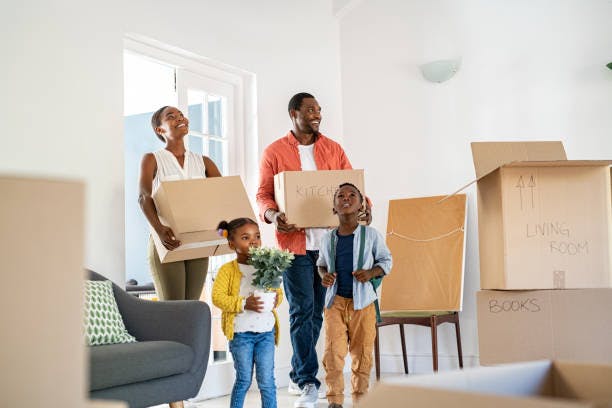 A family with two children carrying moving boxes into a new home