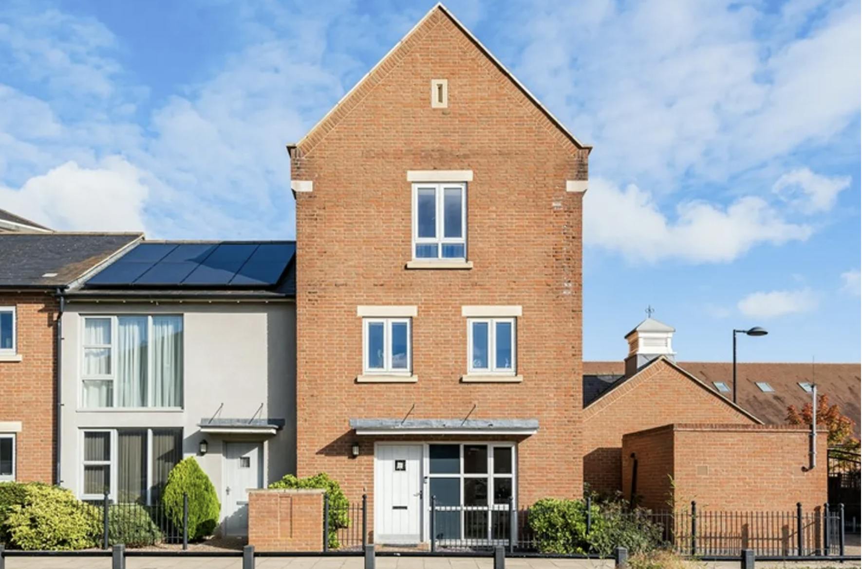 Three storey brick house with a white extension to the left.