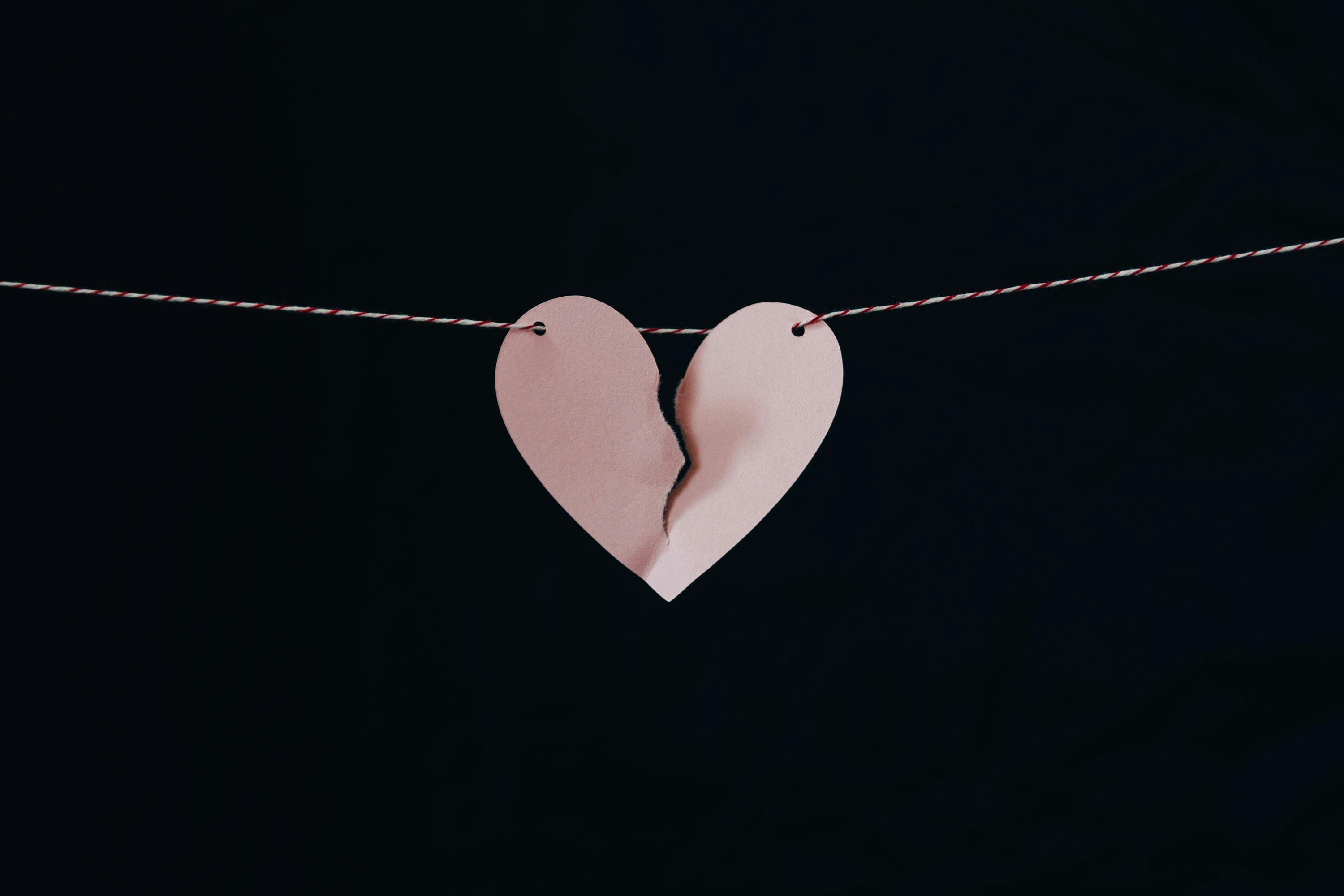 Pink paper heart broken in two, hanging on a string with a black background.