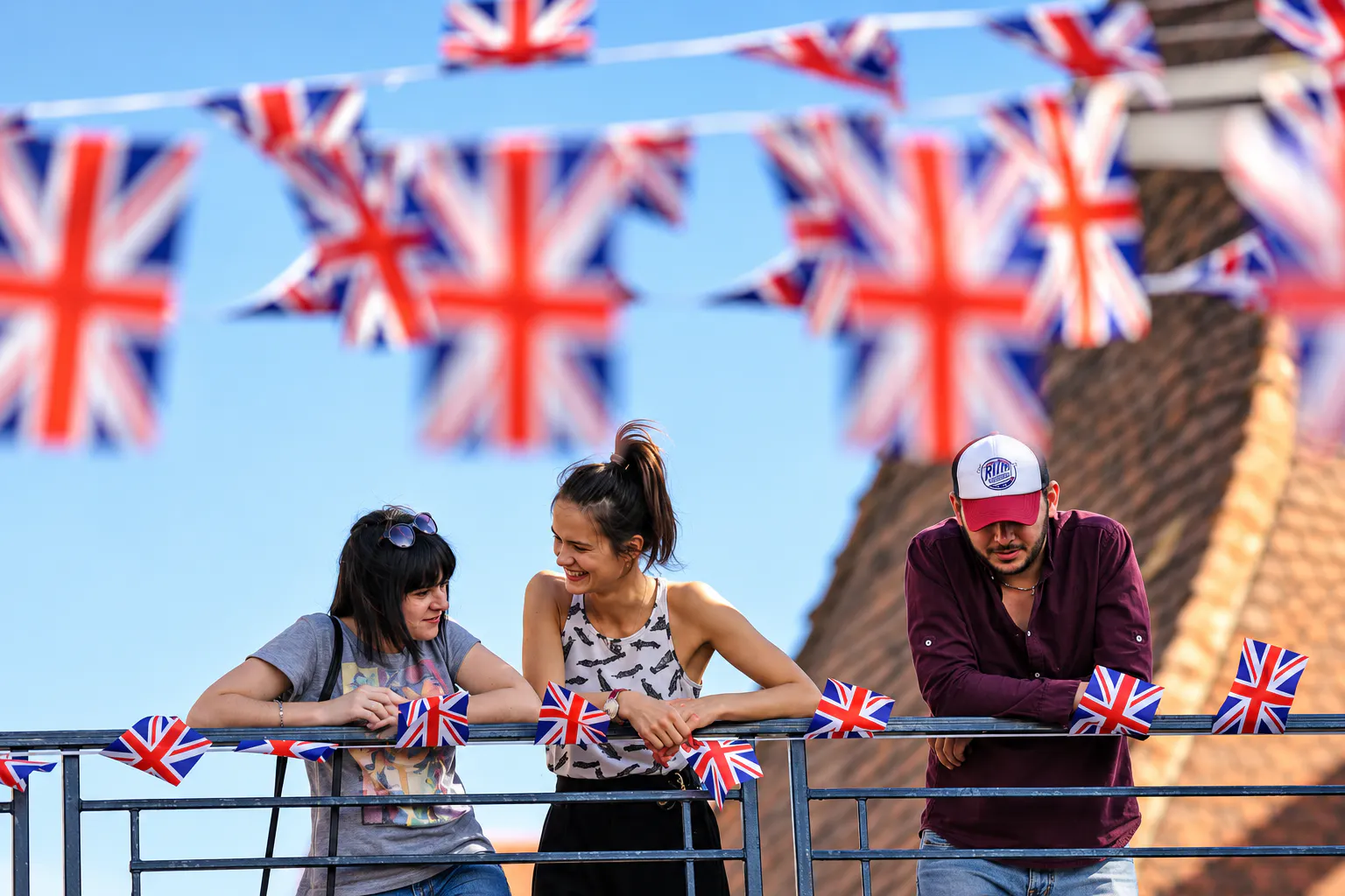 Festival guests leaning on a railing decorated with Union Jack flags under British bunting