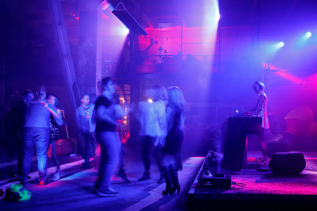 Guests dancing under purple and pink lights in the industrial venue as the DJ plays