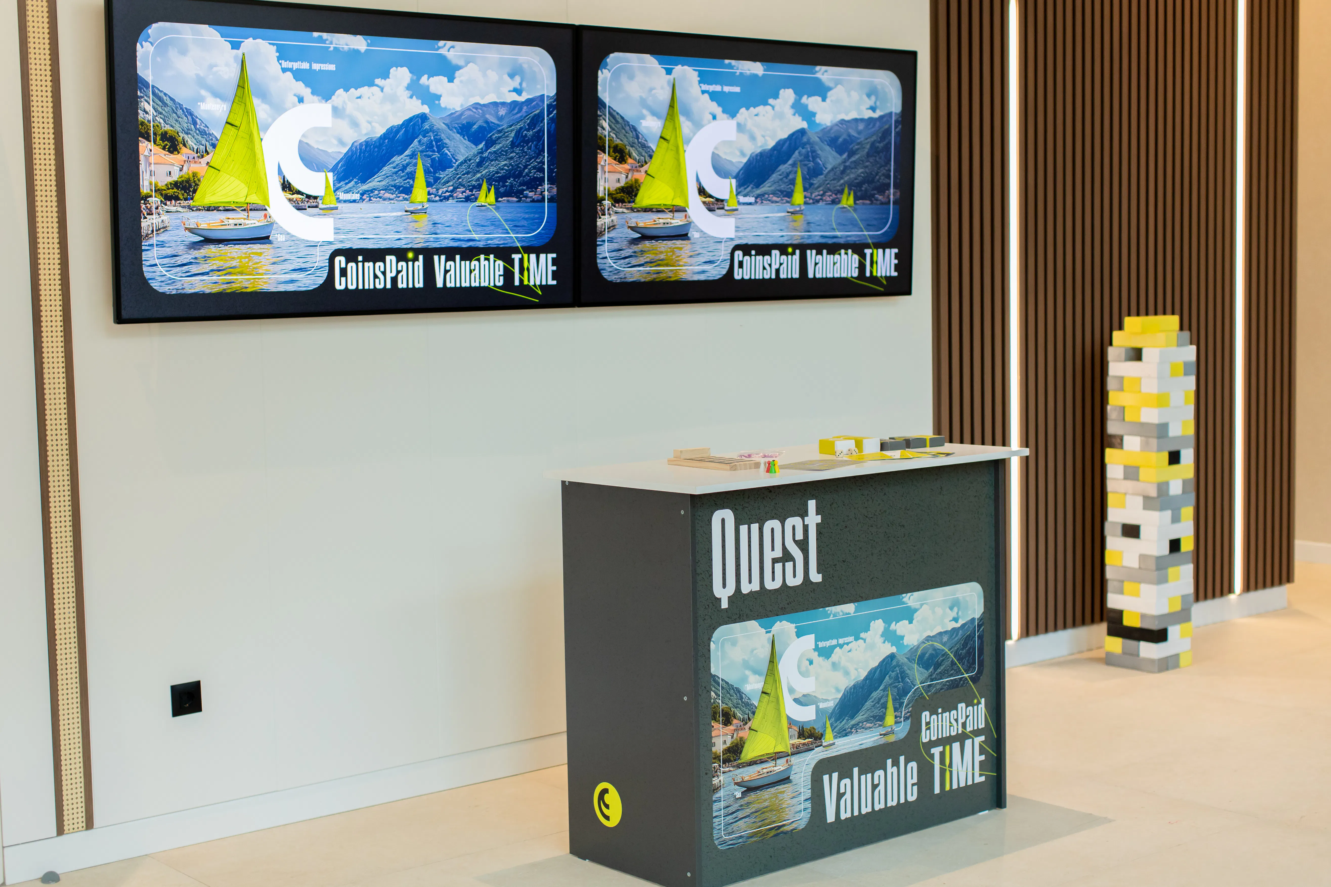 Quest desk and giant yellow-and-grey block tower under CoinsPaid Valuable Time screens