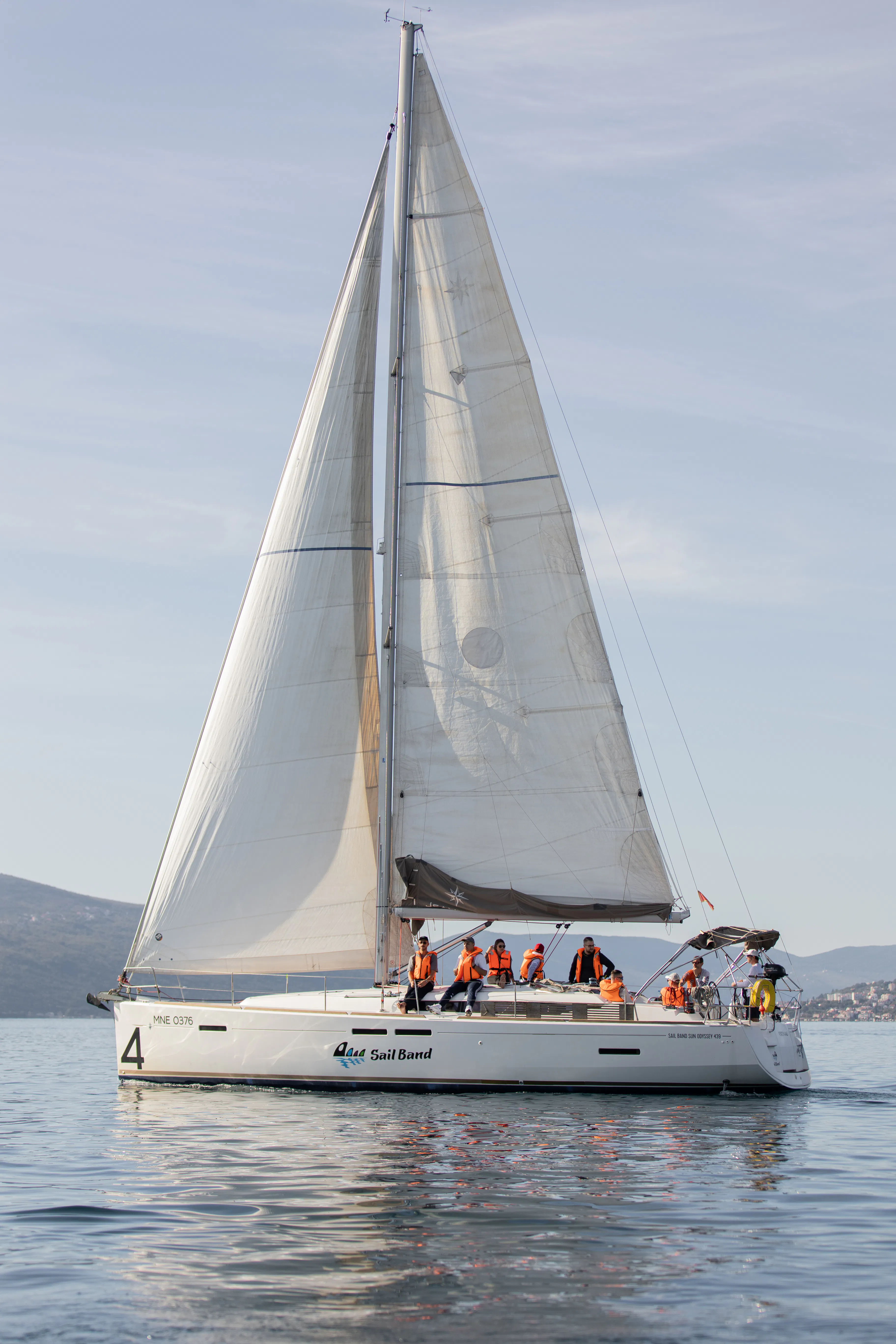 Regatta yacht no. 4 under full sail with a crew in orange life jackets in the Bay of Kotor