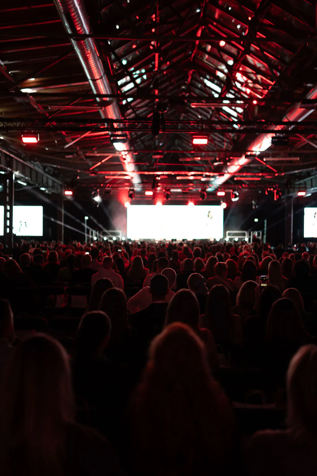 Packed audience facing the main stage LED screens under red-lit roof trusses at Boost Forum Berlin