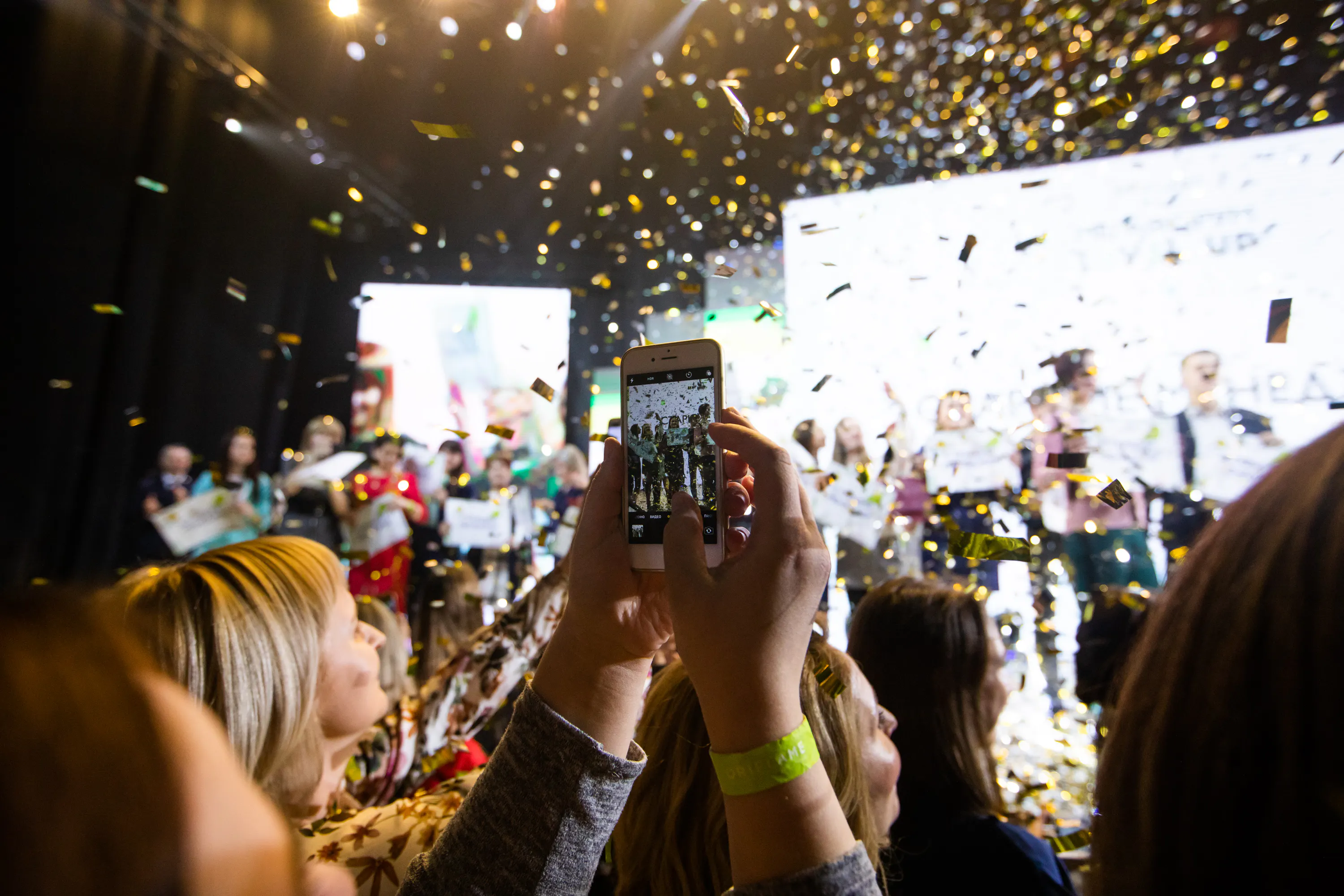 Guest filming the winners on stage with a phone as gold confetti falls over the Oriflame gala crowd