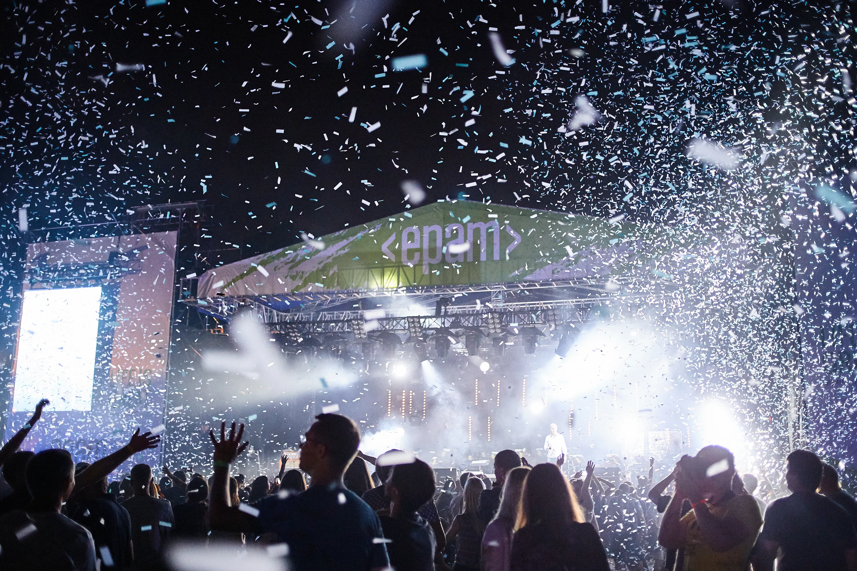 Crowd cheering under a confetti shower in front of an outdoor EPAM-branded concert stage at night