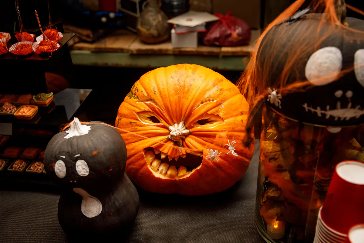 Carved jack-o'-lantern with plastic spiders beside black pumpkins painted as ghosts