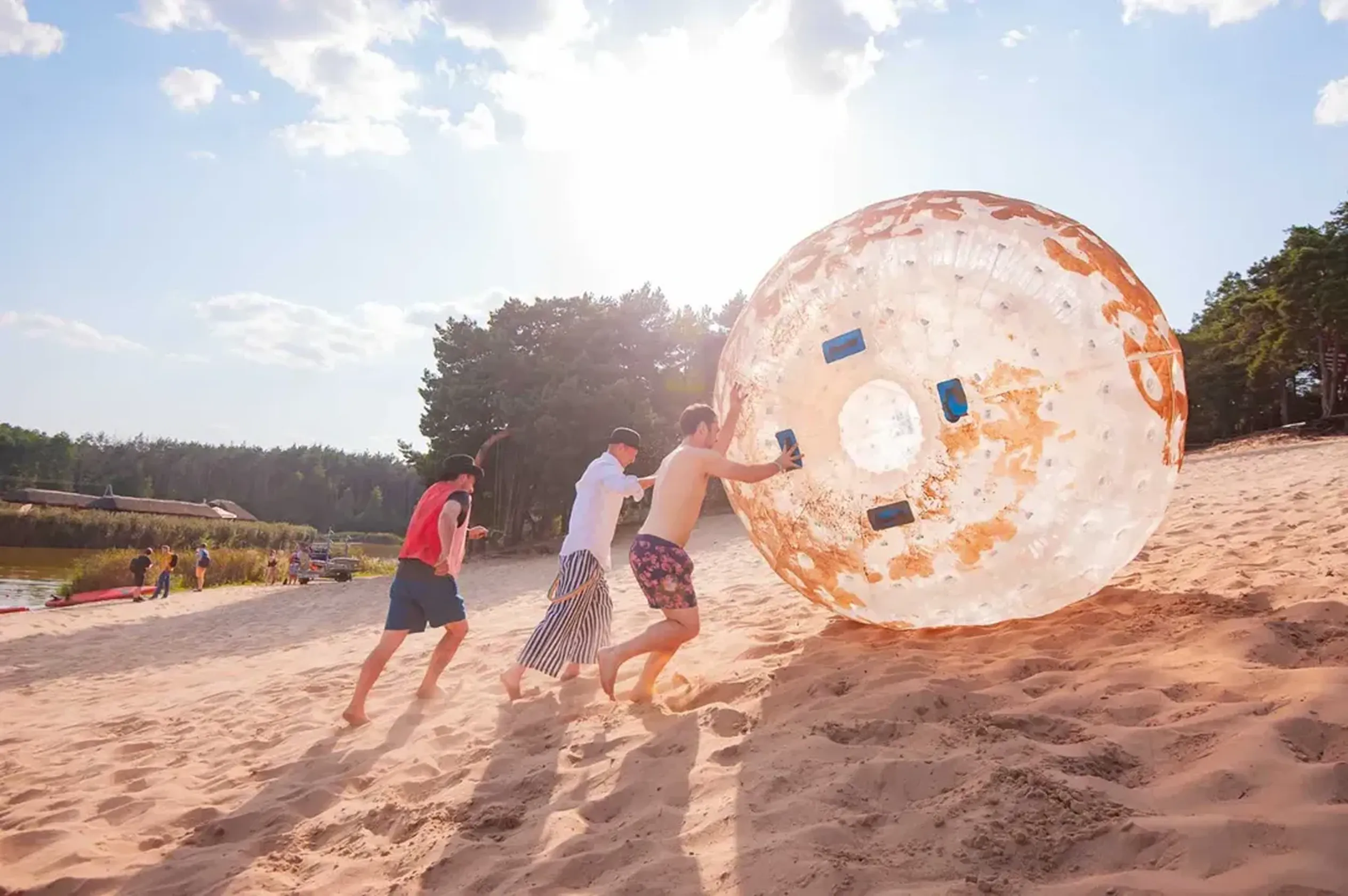 Godel employees pushing a giant inflatable zorb ball across a sunny sandy beach by the lake