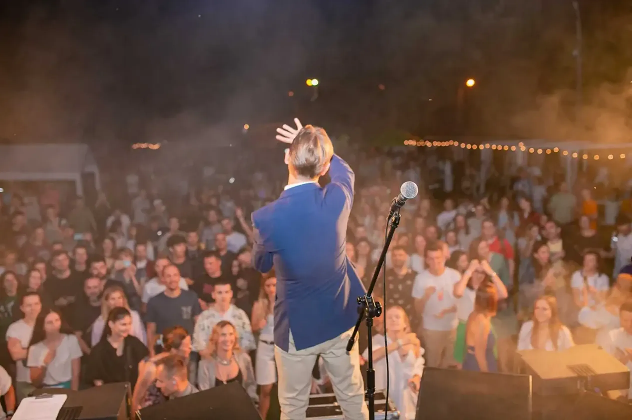 Singer on stage greeting the crowd at the Godel evening music party under string lights