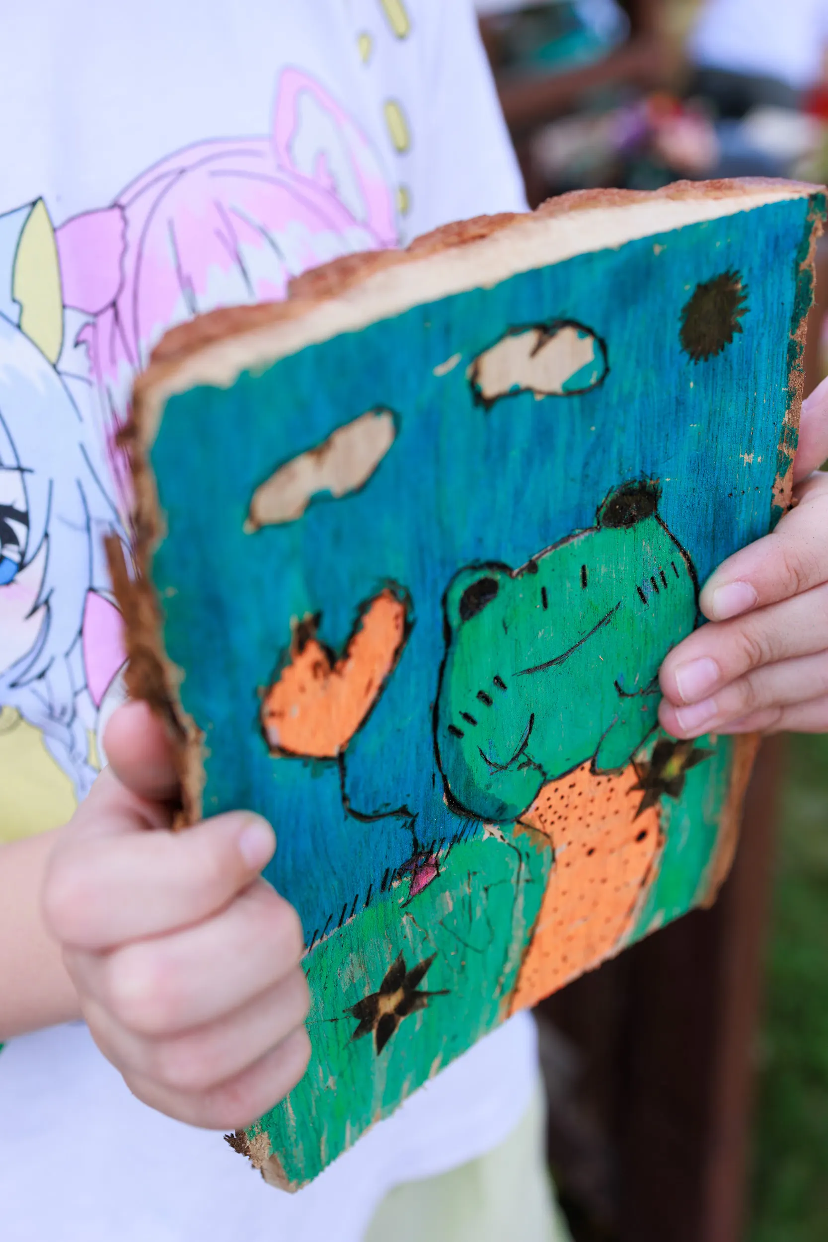 Child holding a painted wood-burning artwork made during a creative workshop at SOFTSWISS Kids Camp