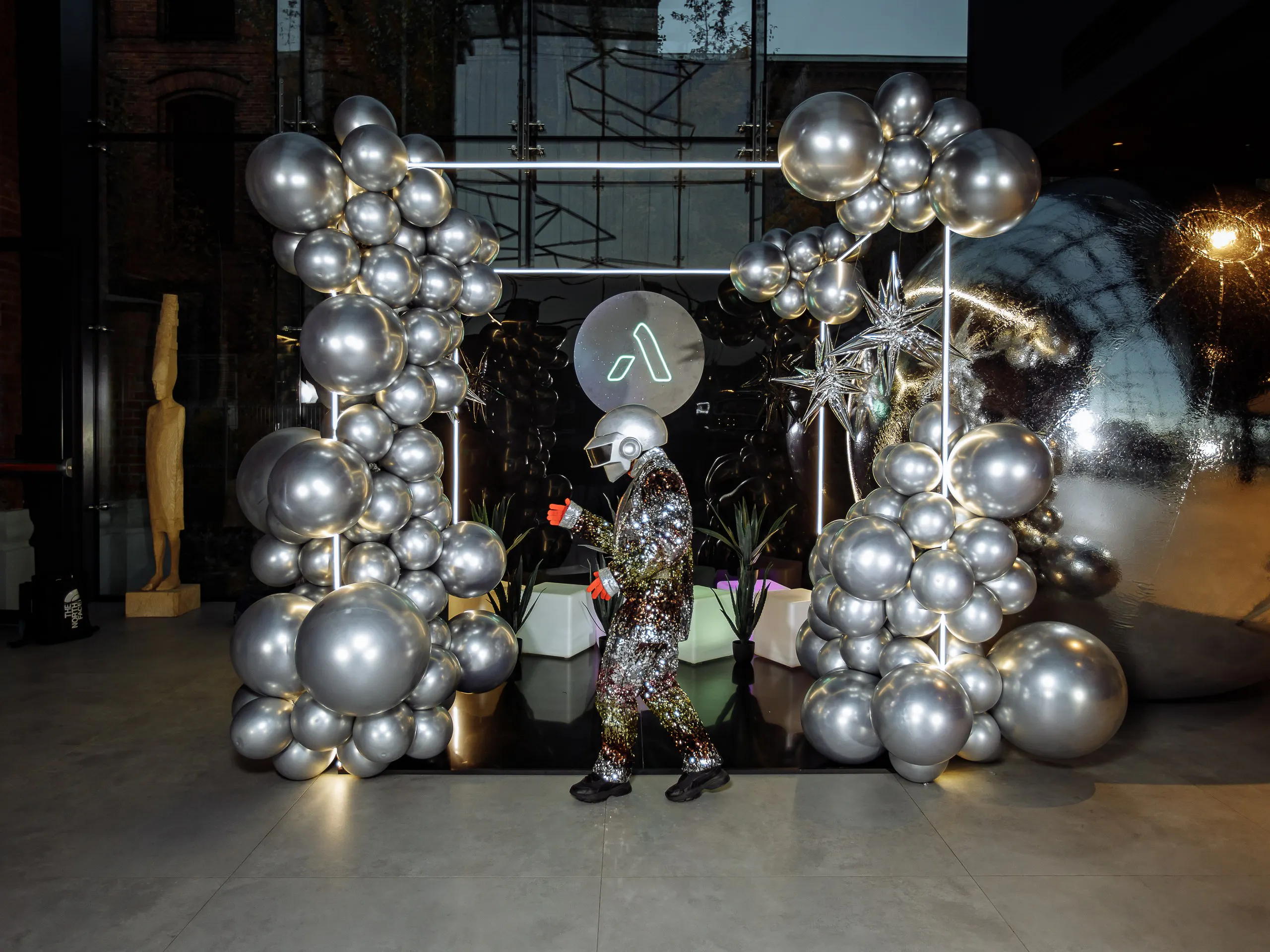 Performer in a sequin suit and helmet by a silver balloon installation at the Astek Constellation gala
