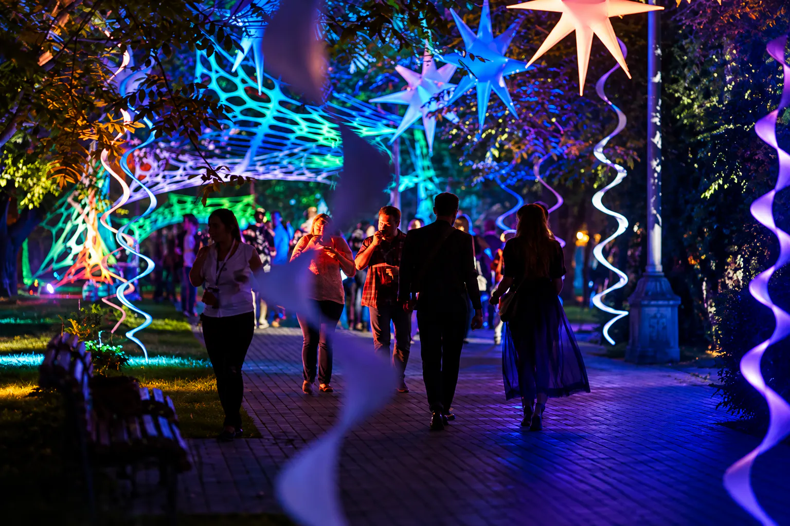 Guests strolling along a park alley lit by neon light installations and glowing inflatable stars