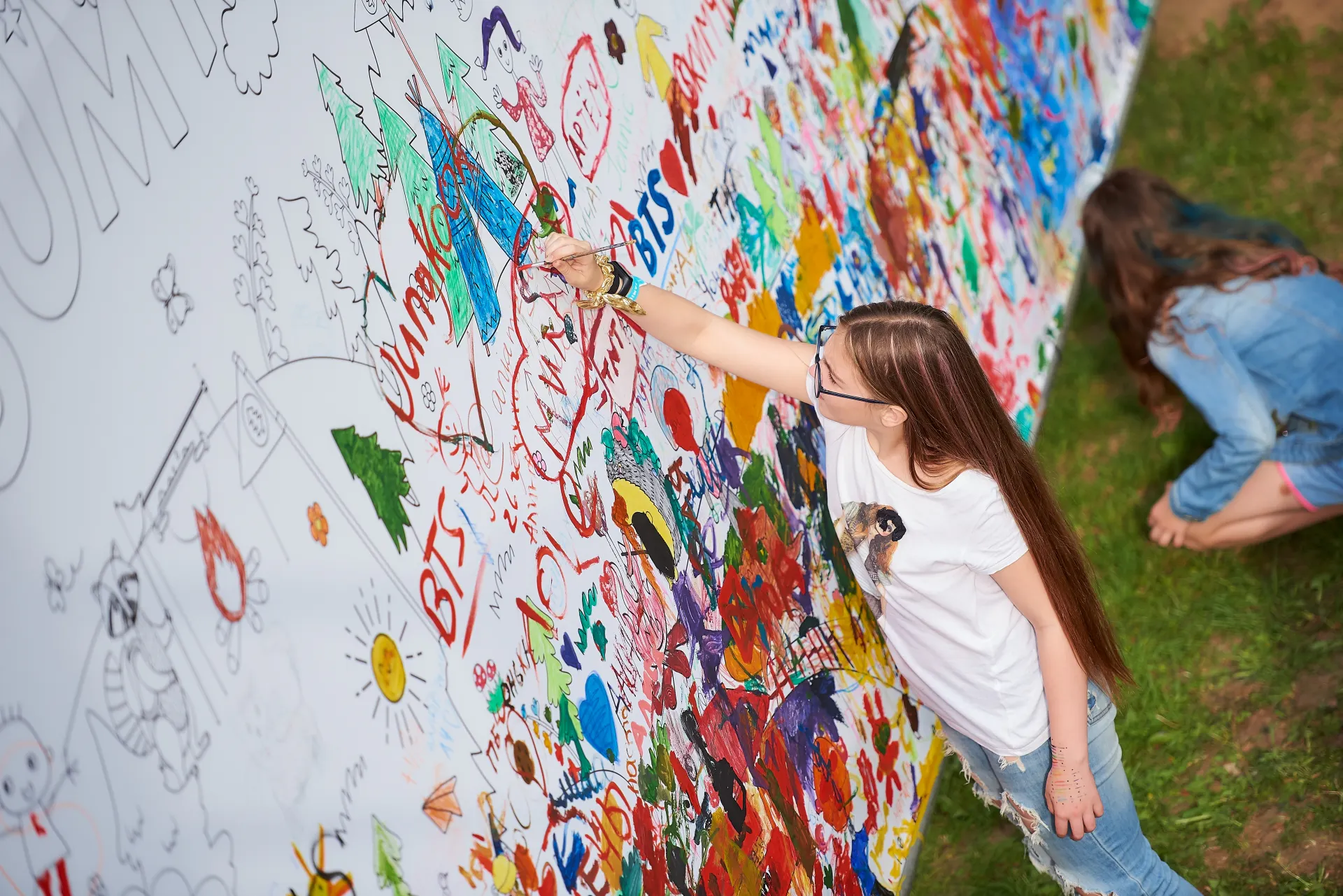 Girl painting on a giant coloring wall covered in children's drawings
