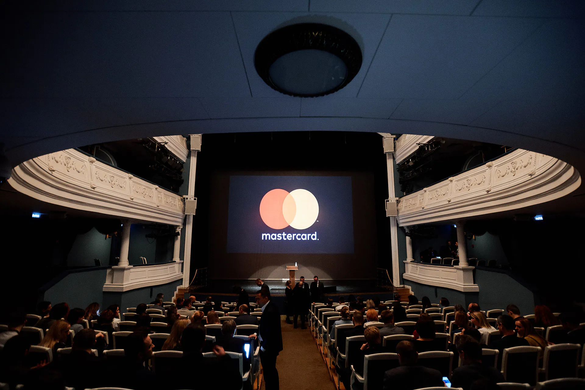 Theatre hall with ornate balconies and the Mastercard logo on the stage screen as Masterday guests take their seats