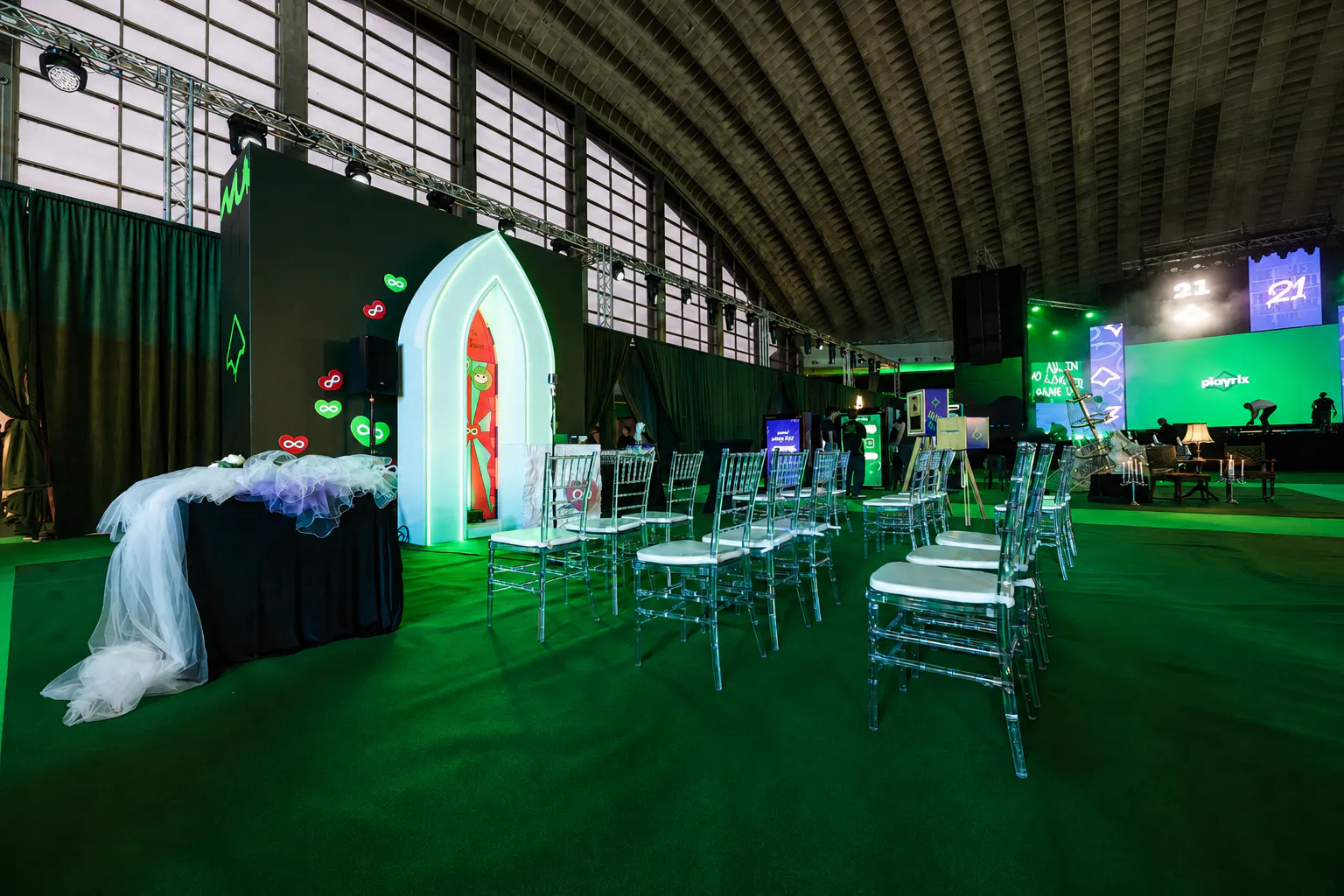 Neon-lit arched chapel doorway with acrylic chairs, a veiled table and the Playrix stage behind