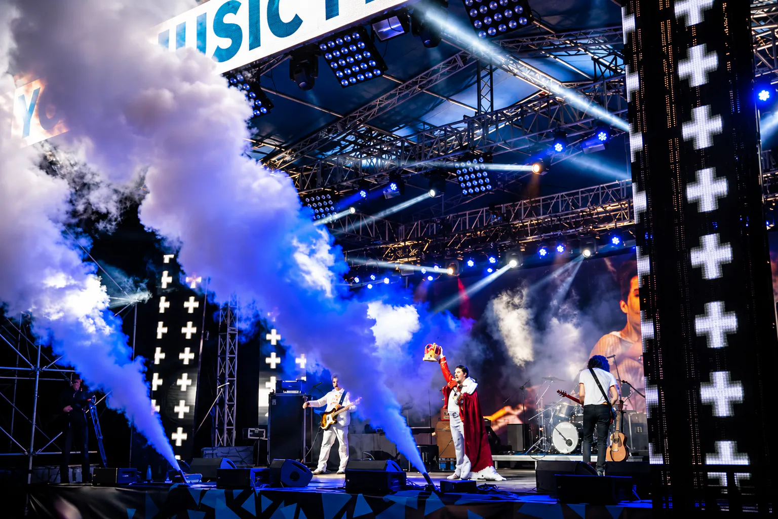 Performer in a red royal cape raising a crown on stage as CO2 jets fire at Your Music Fest