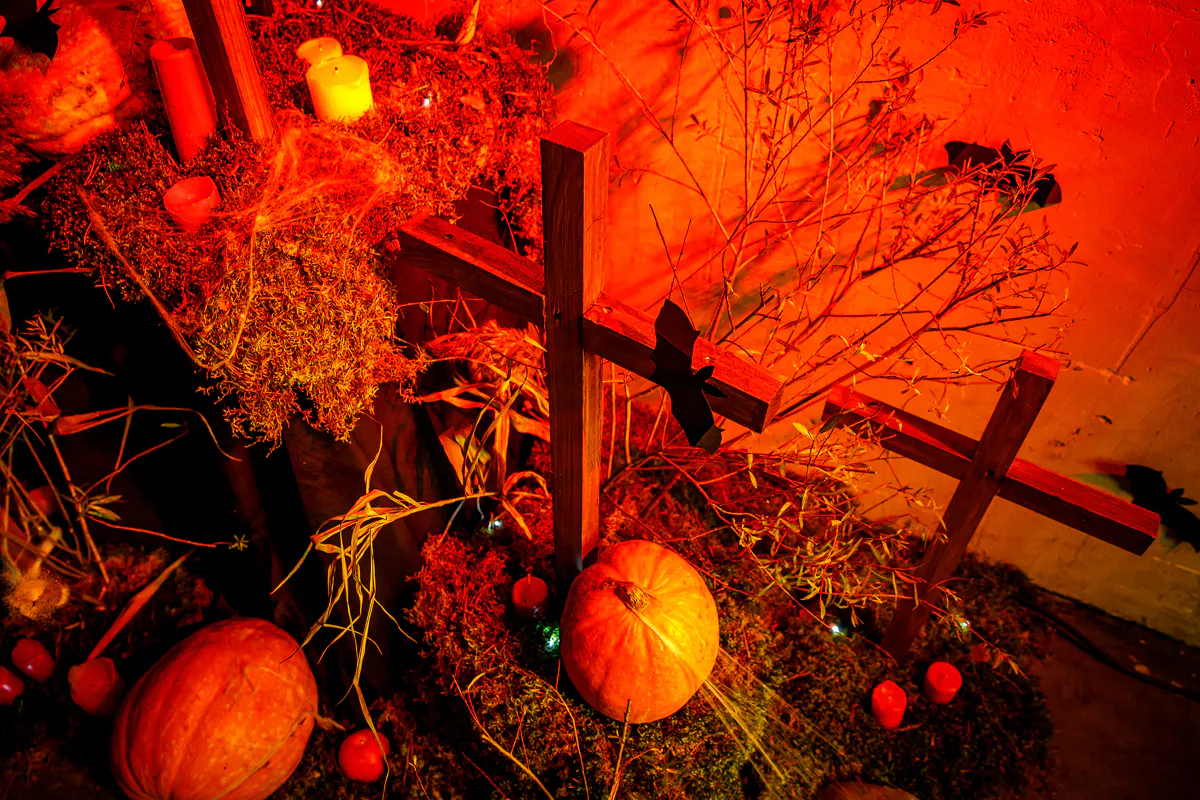 Graveyard installation with wooden crosses, pumpkins and candles lit in red