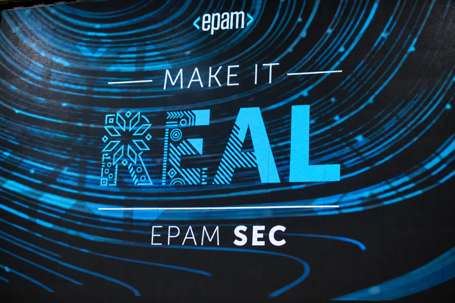 LED screen with the EPAM SEC "Make It Real" conference key visual in blue light trails