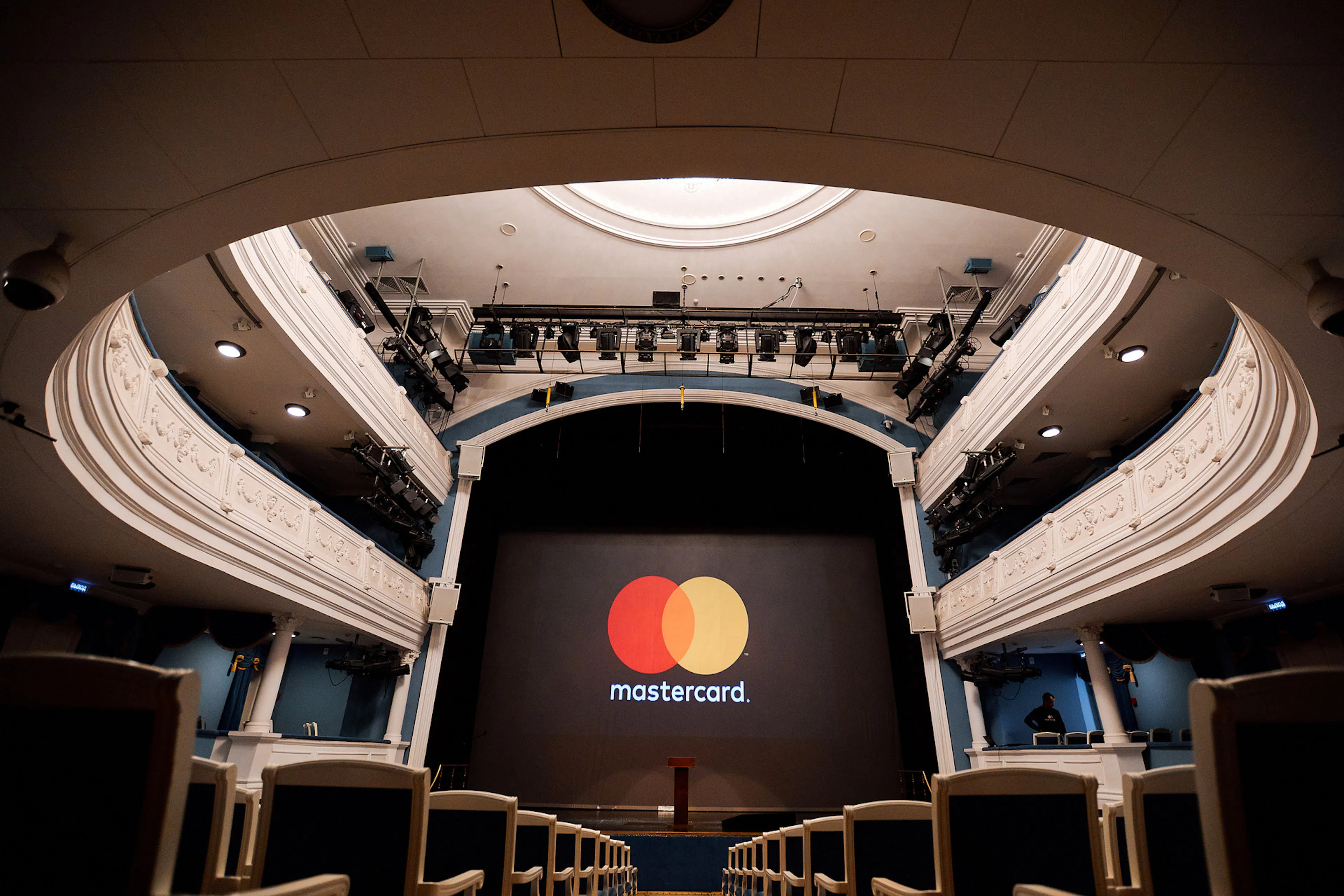 Logo Mastercard na ekranie sceny w otoczeniu zdobionych balkonów teatru i oświetlenia scenicznego