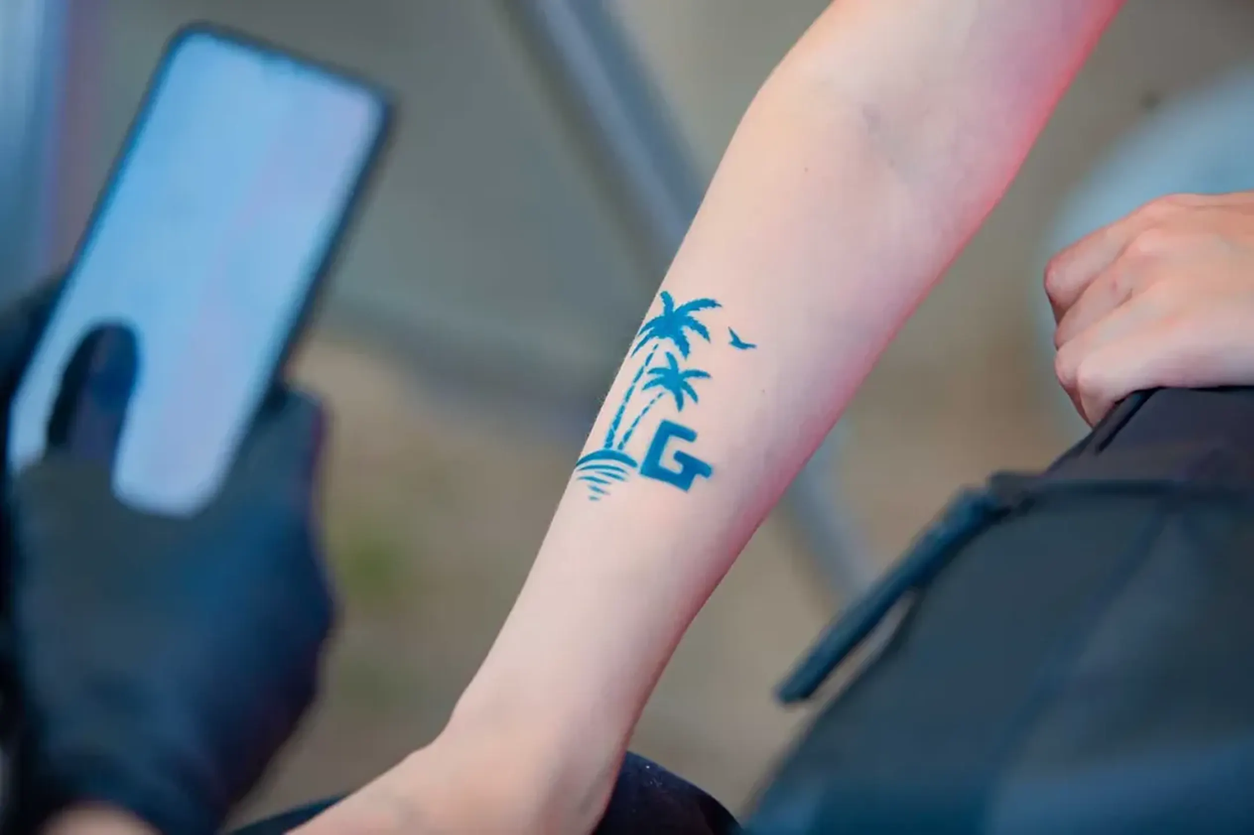 Temporary tattoo with the Godel G logo and palm trees on a guest's forearm