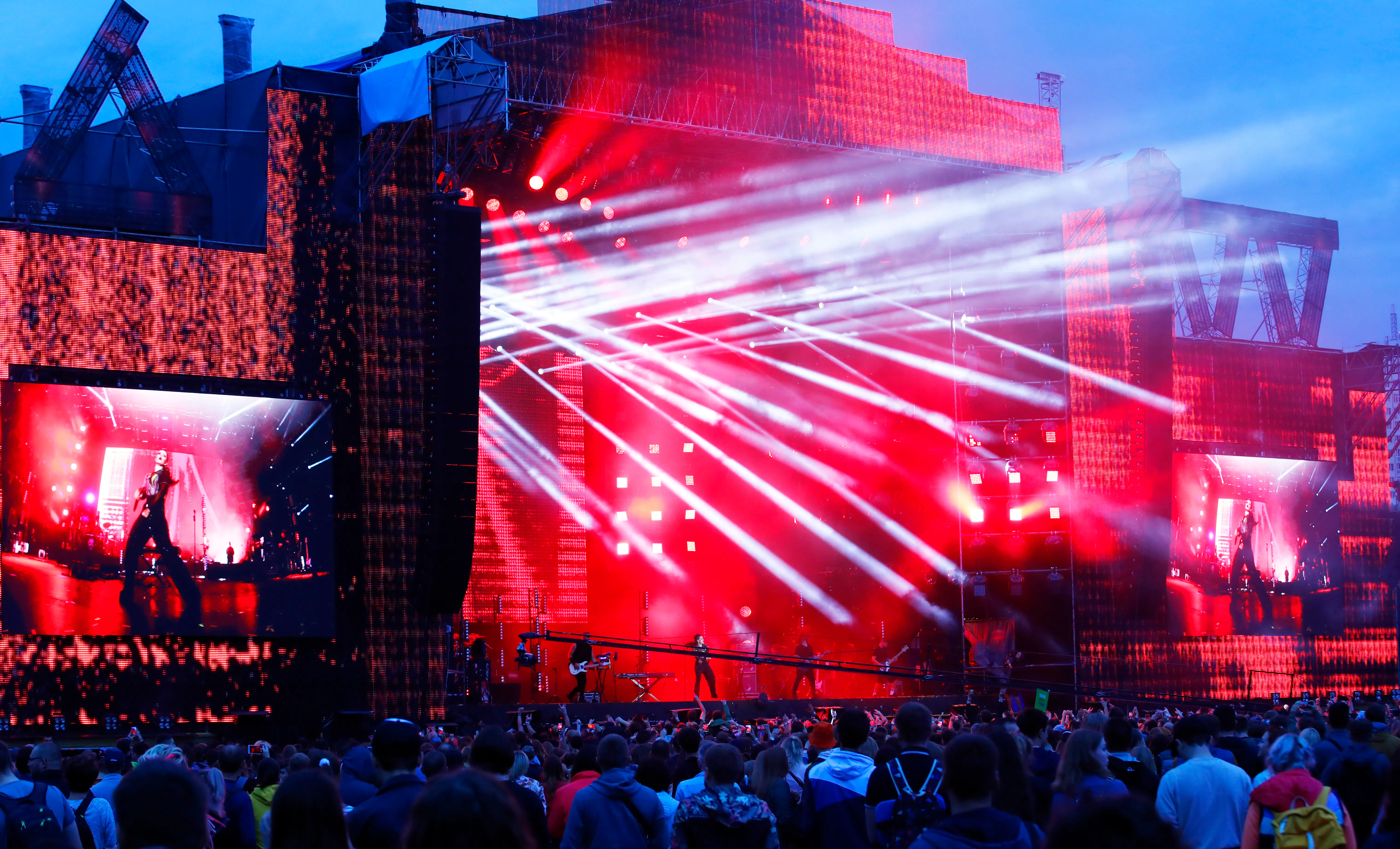 Festival crowd facing the Atlas Weekend main stage with red LED walls, giant screens and white light beams
