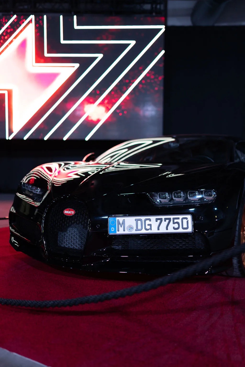 Black Bugatti supercar displayed on a red carpet in front of an LED wall at Boost Forum Berlin
