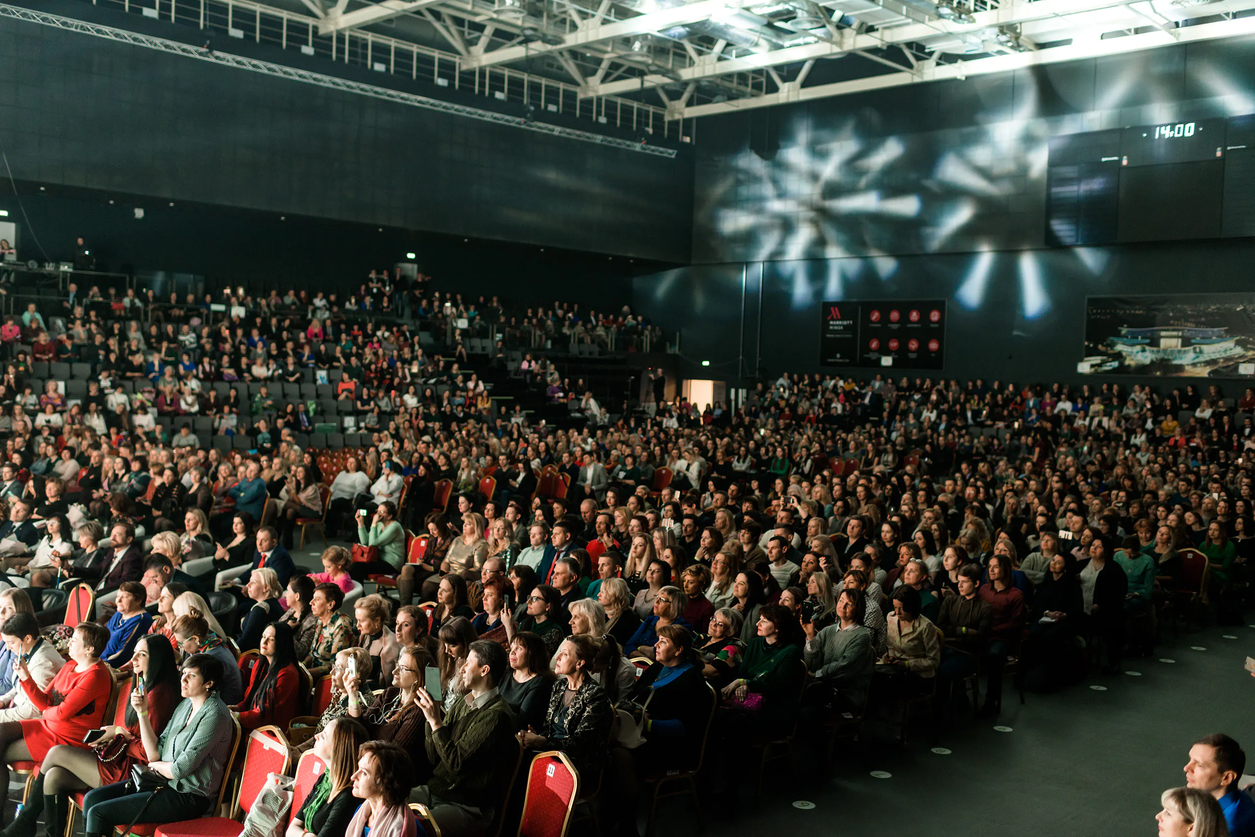 Full arena audience watching the Oriflame Summit, with light projections on the walls