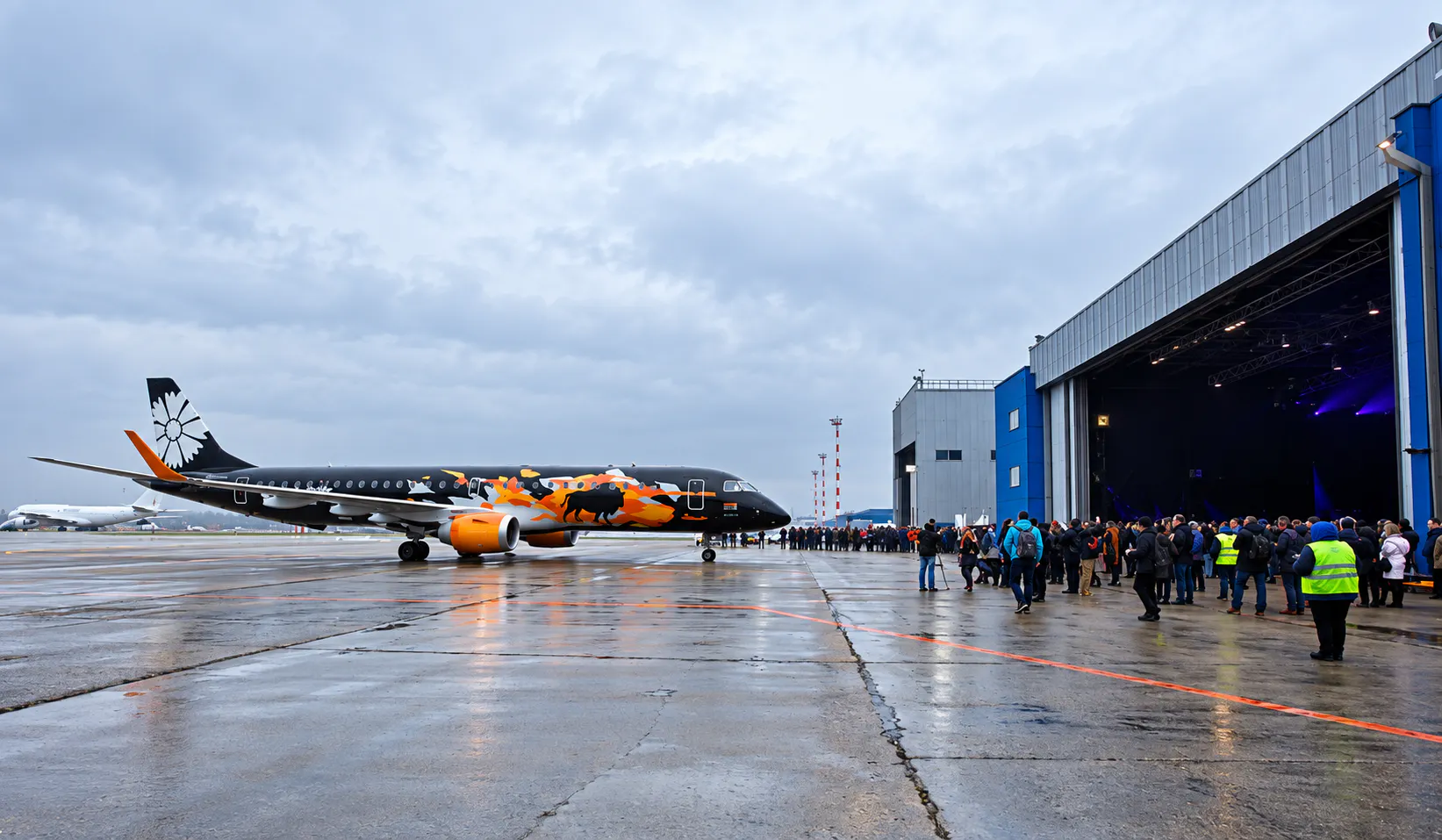 Tankolet 2.0 aircraft on a wet apron as guests gather outside the open, stage-lit hangar