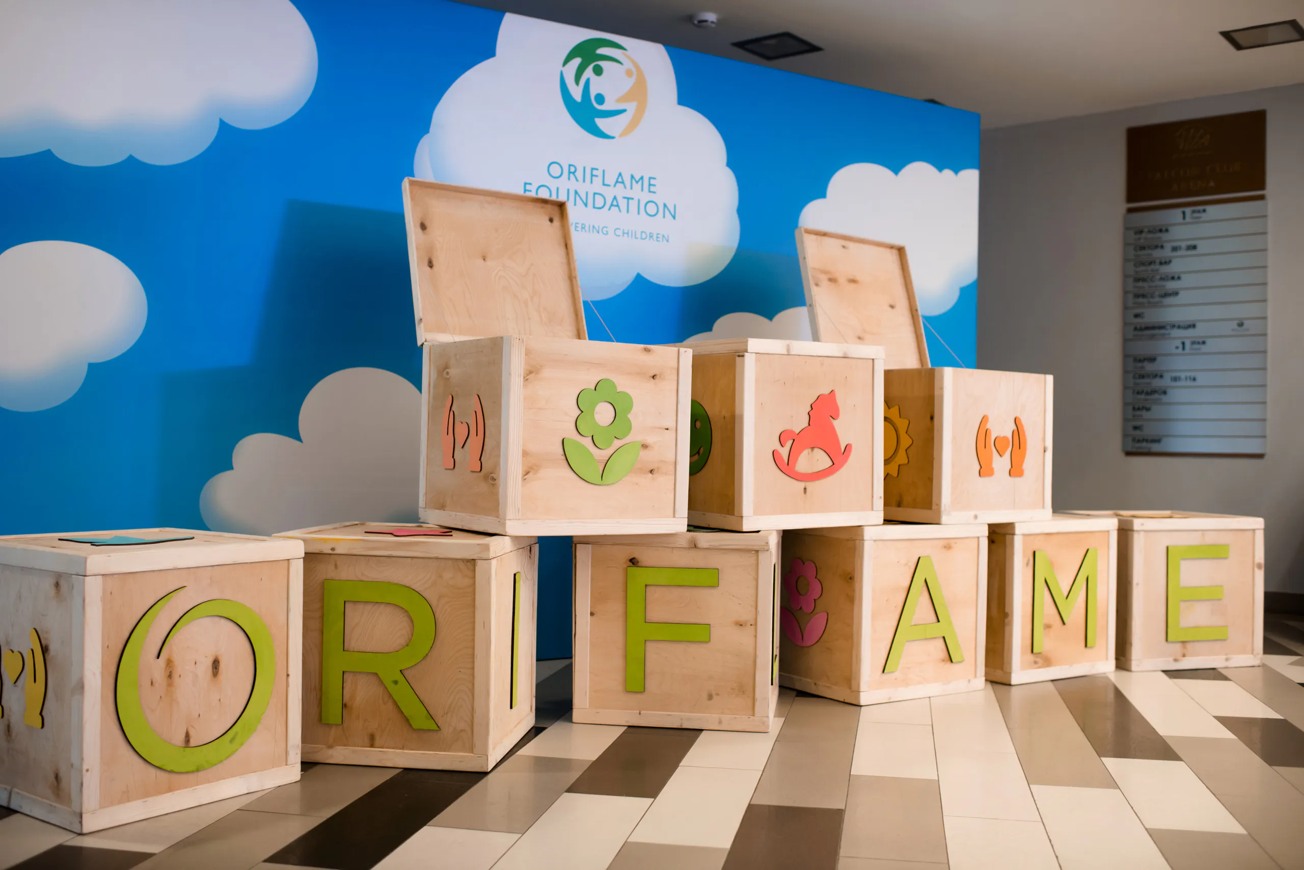 Wooden boxes spelling Oriflame in front of an Oriflame Foundation backdrop with clouds