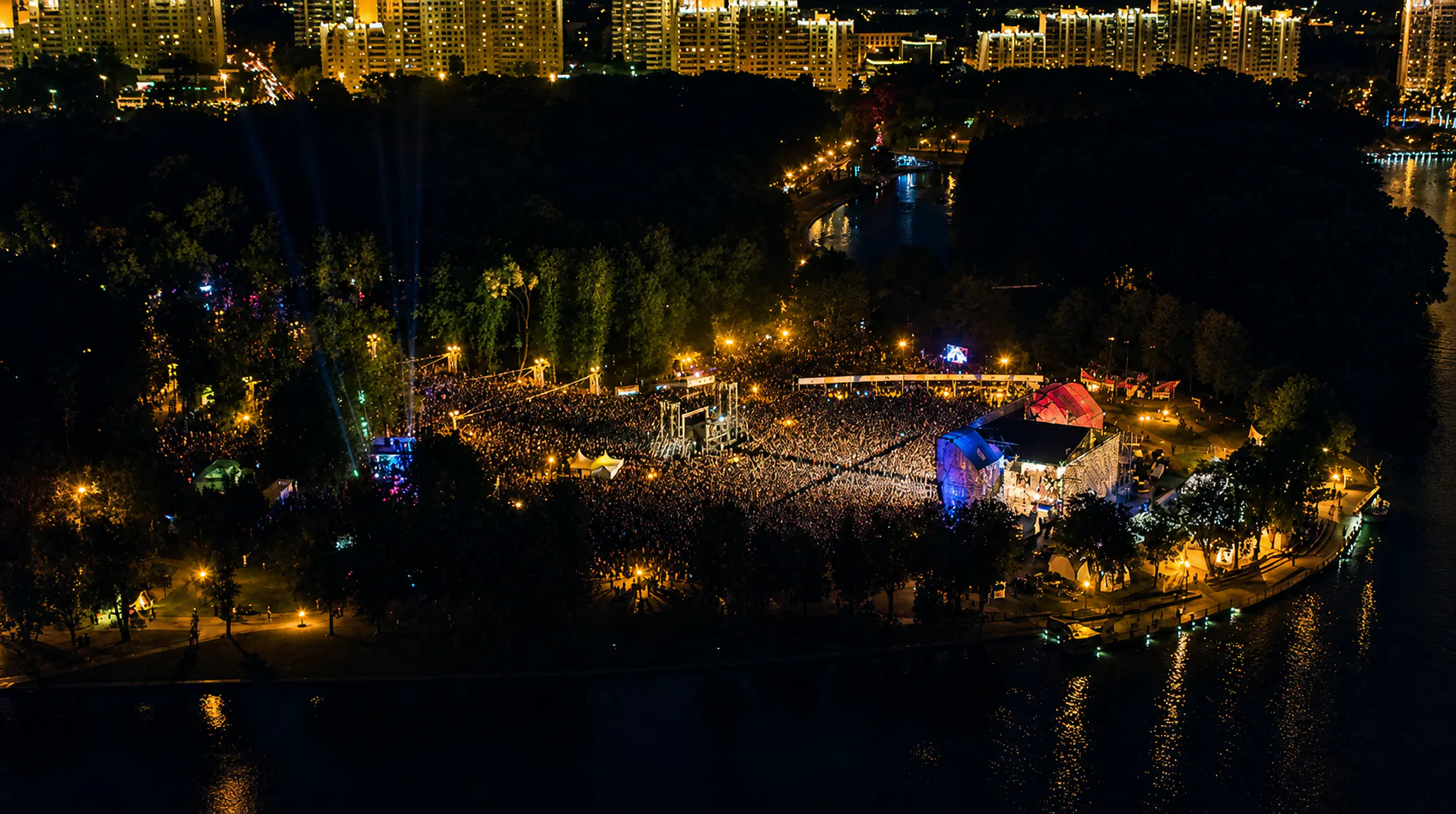 Aerial night view of the Wargaming Fest crowd and stages in a riverside city park