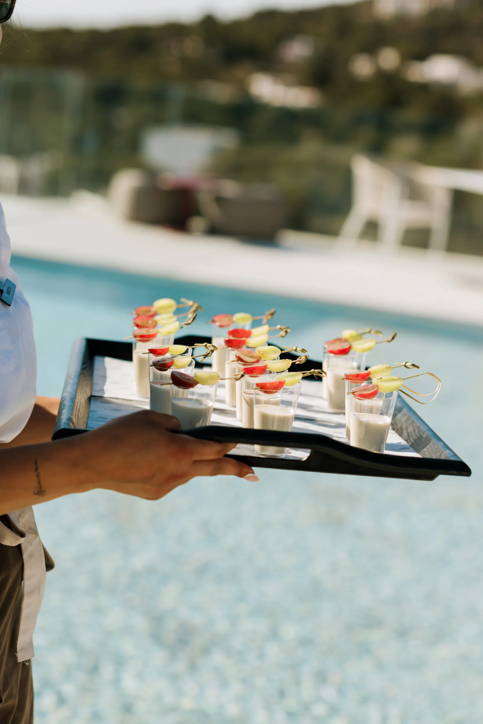 Waiter serving welcome appetizer shots with grape skewers by the pool