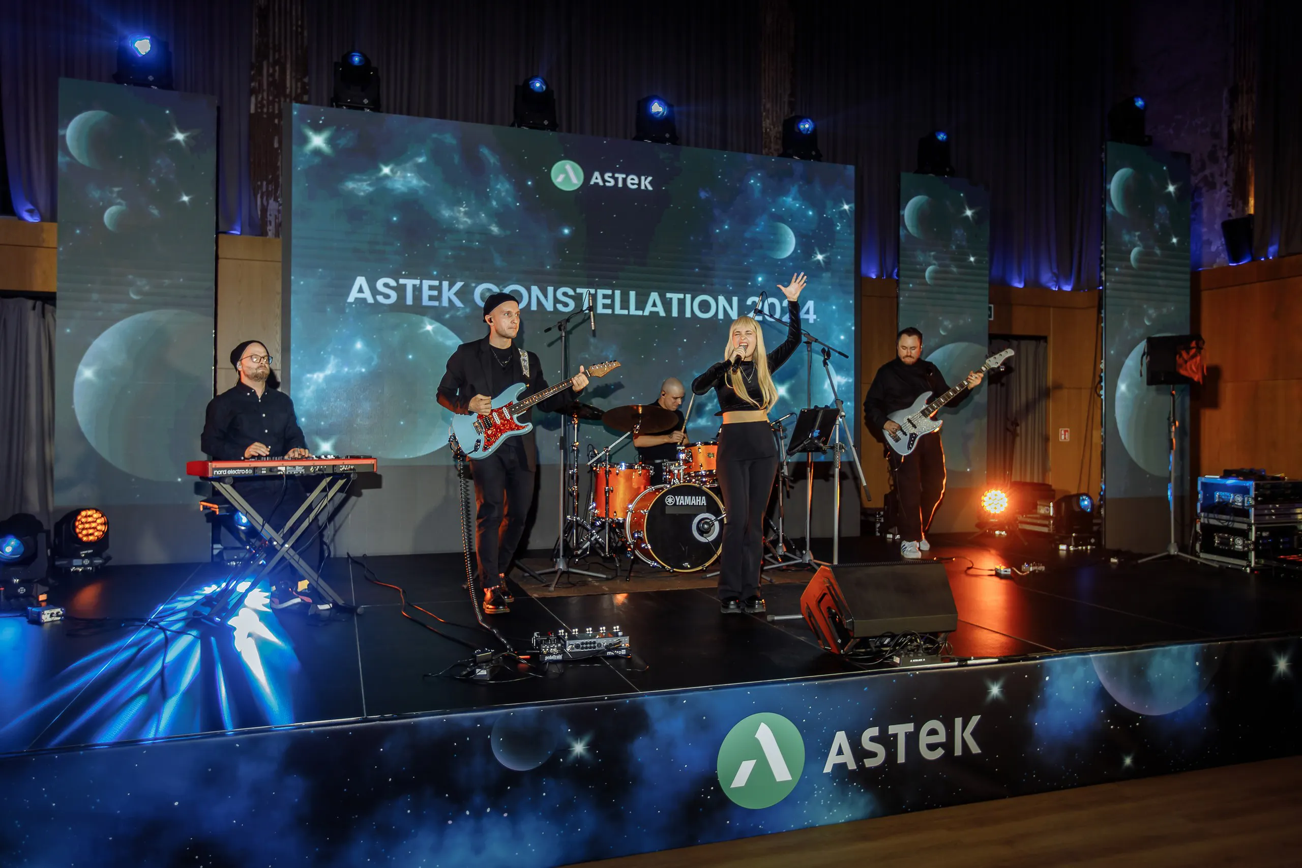 Live band on the Astek-branded stage with ASTEK CONSTELLATION 2024 on the LED screen