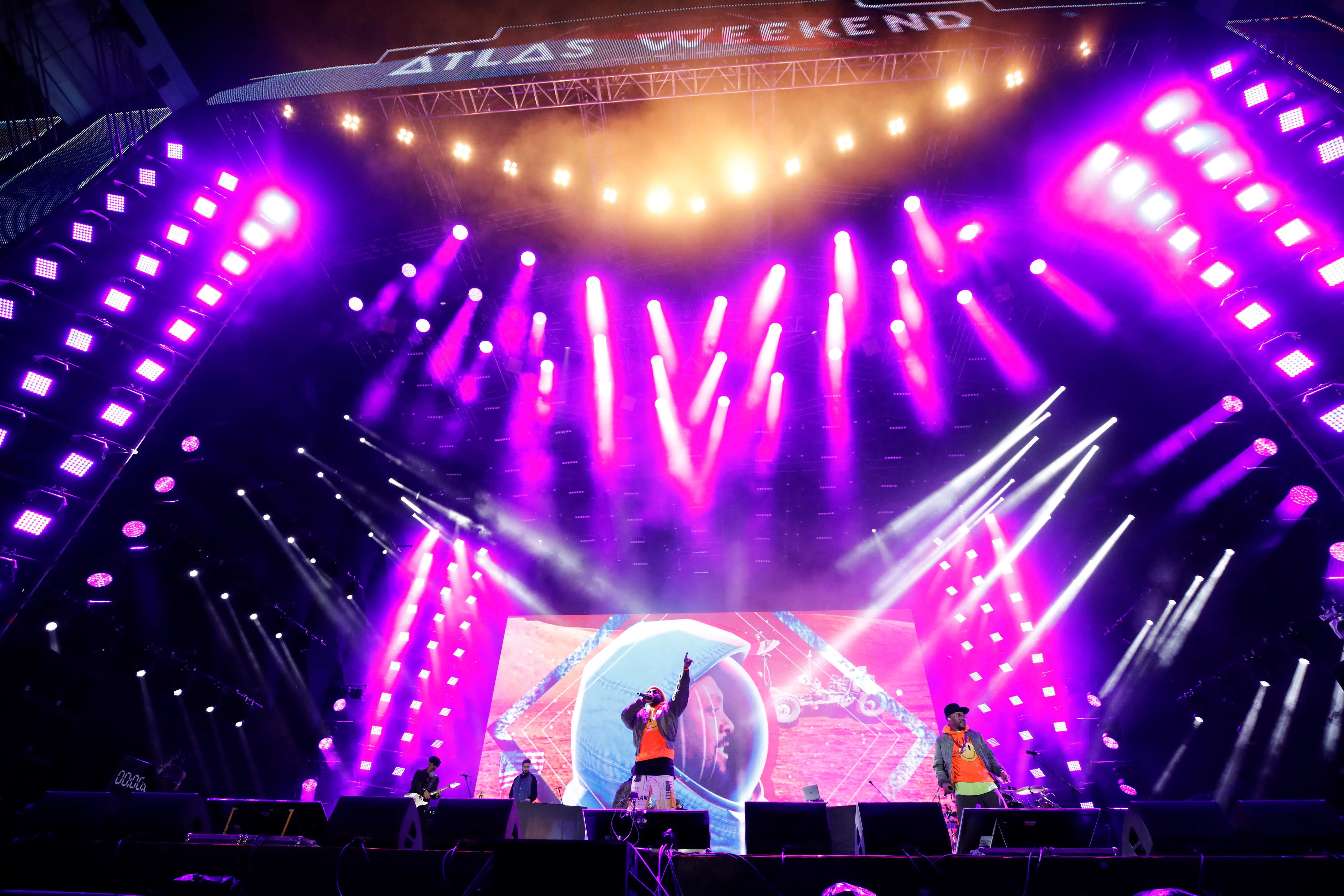 Atlas Weekend stage lit with purple and white moving-head beams above performers and a large LED screen