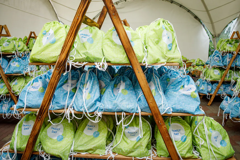 Wooden racks stacked with green and blue Family Day drawstring gift bags