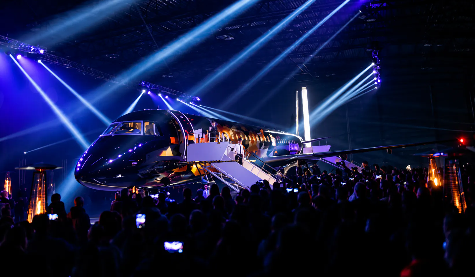 Guests filming the Tankolet 2.0 aircraft reveal in a dark hangar lit by blue beams and patio heaters