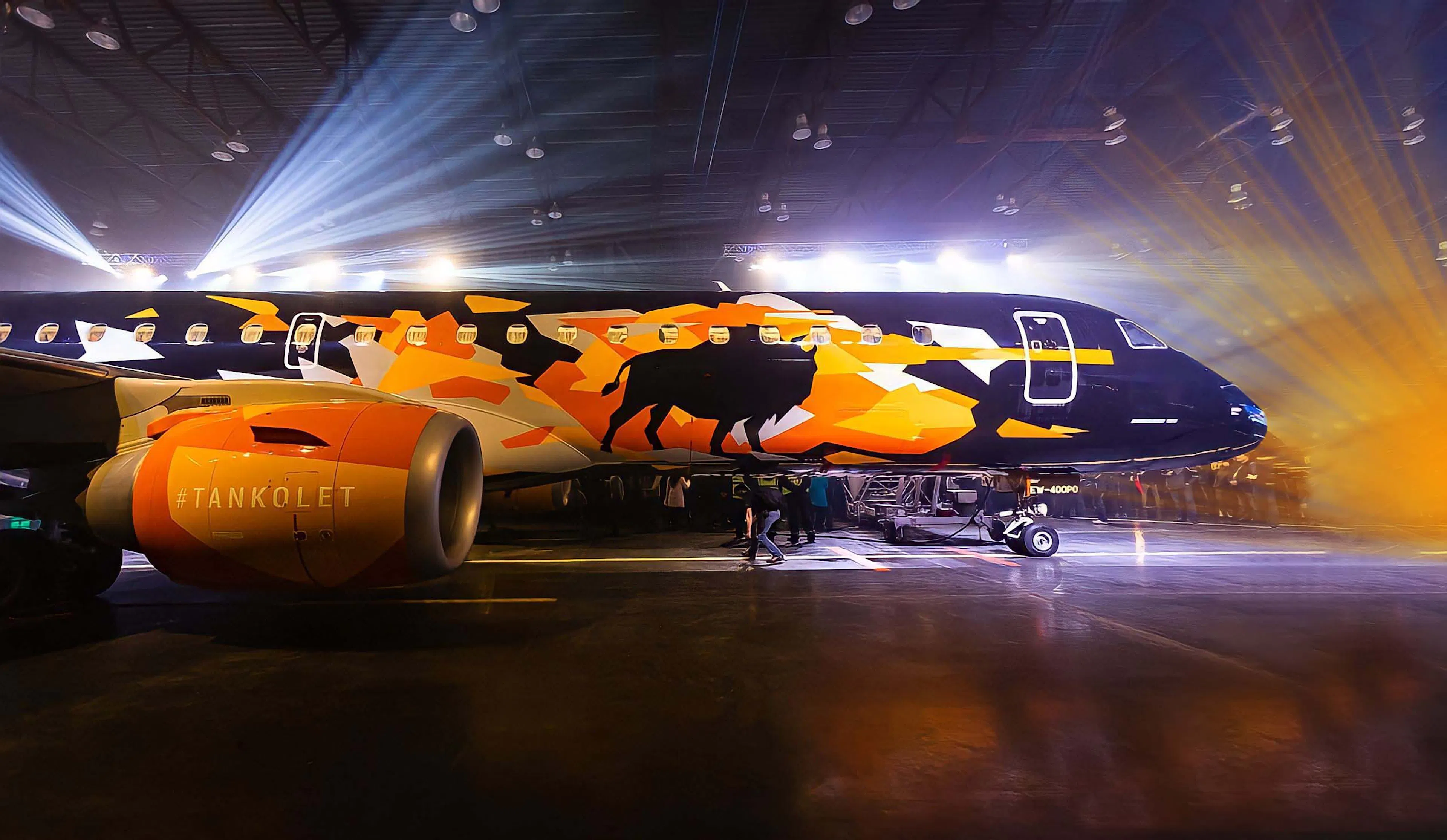 Samolot Embraer Tankolet w czarnym malowaniu z pomarańczowym motywem żubra w snopach światła w hangarze
