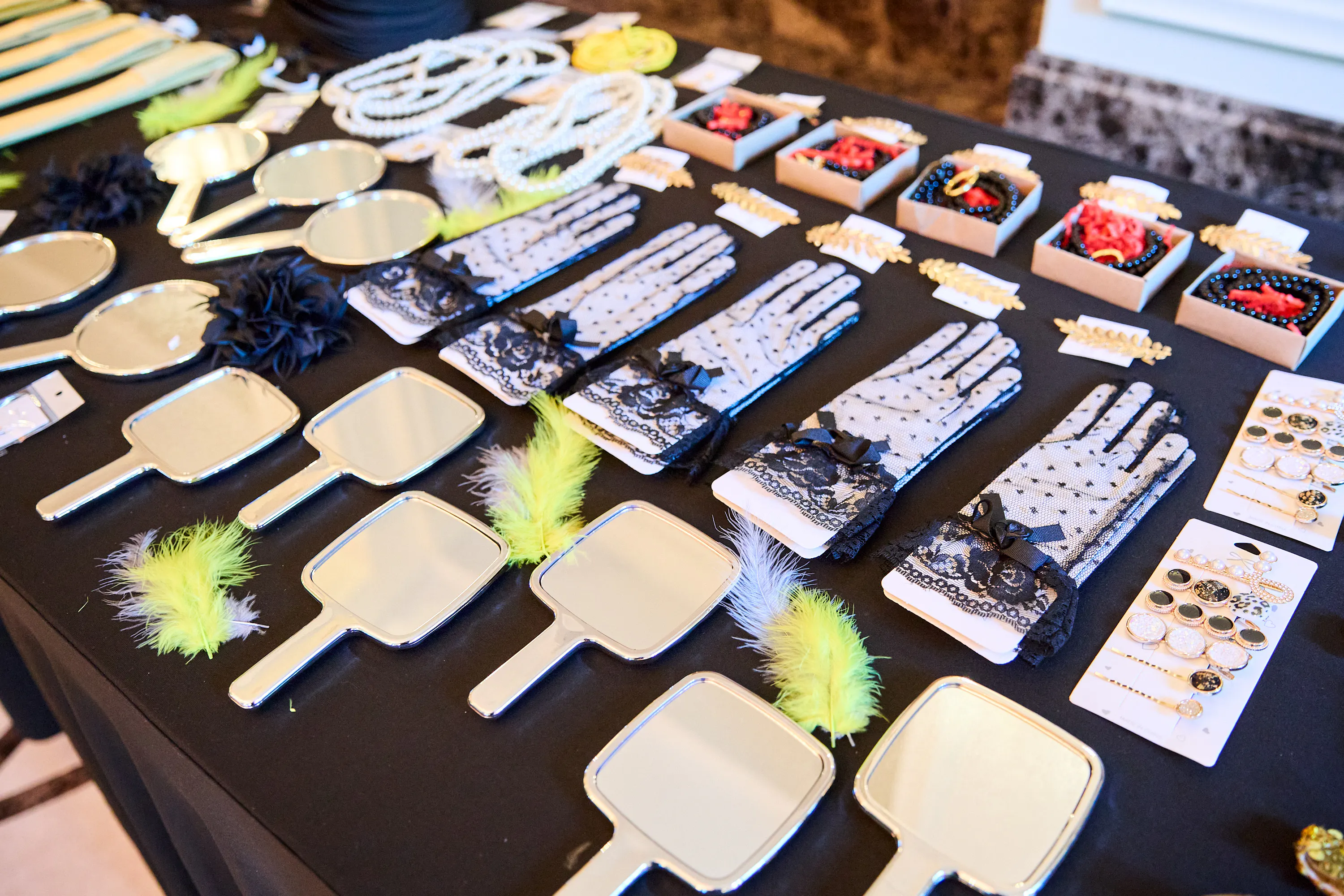 Vintage accessories for guests: hand mirrors, lace gloves, pearls and feathers laid out on a table