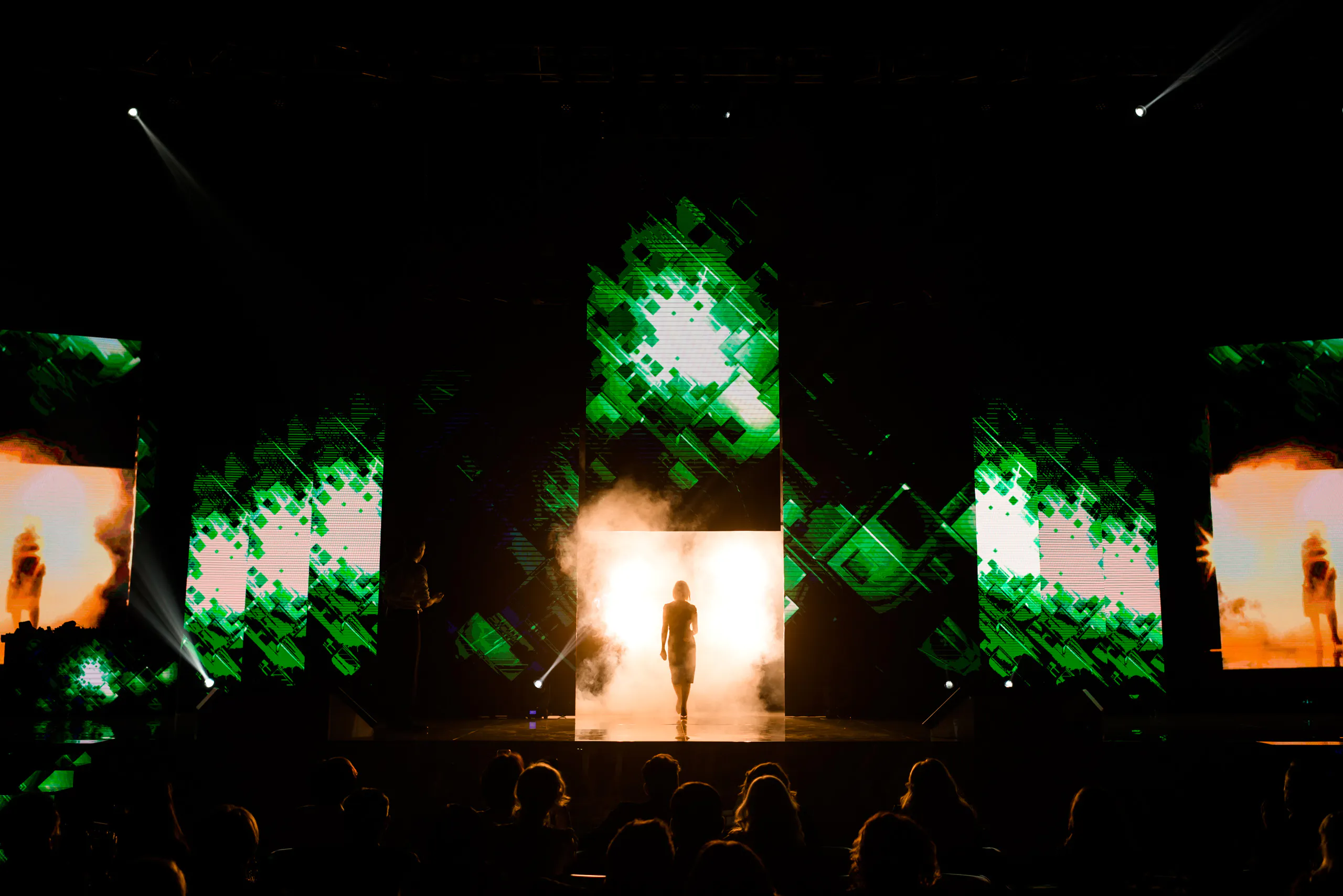 Silhouette walking out through stage smoke framed by green LED screens at the Oriflame gala