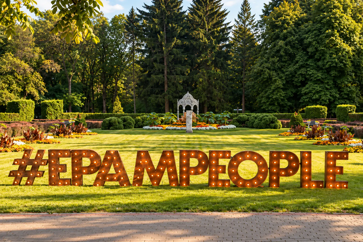 Illuminated marquee letters spelling #EPAMPEOPLE on a manicured park lawn