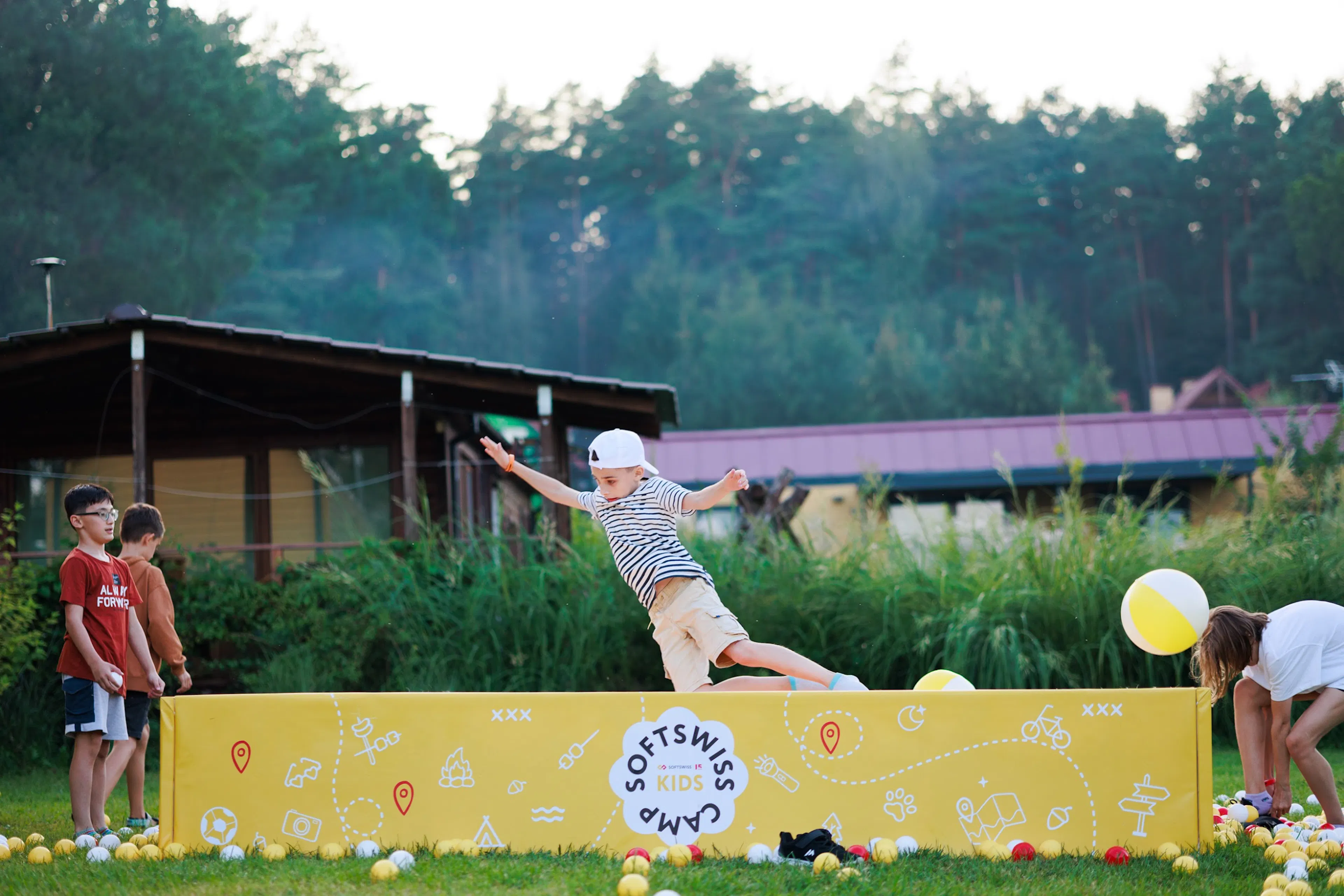 Chłopiec przeskakujący żółtą barierkę SOFTSWISS Kids Camp podczas gier na świeżym powietrzu