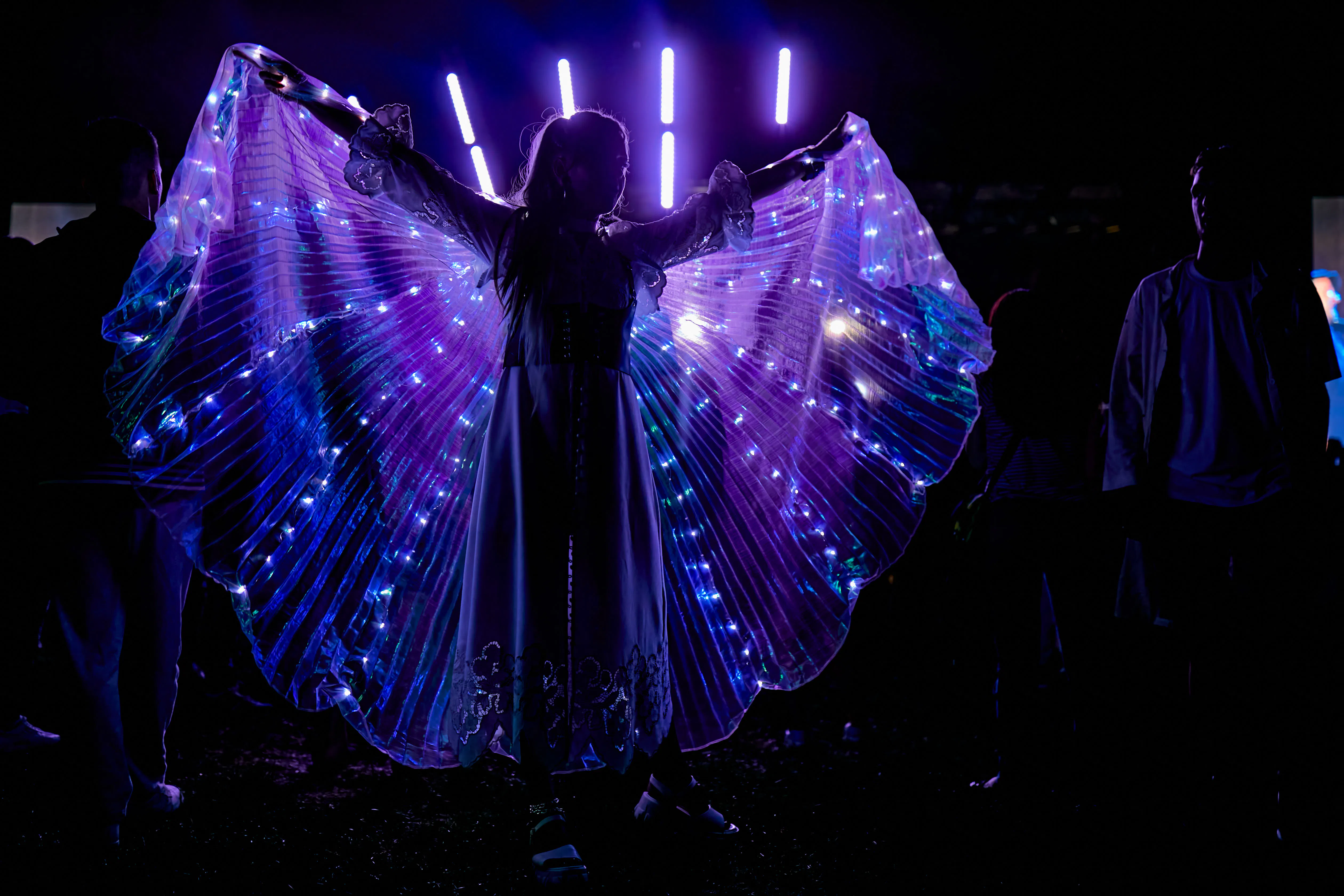 Festival guest spreading glowing LED light-up wings in the dark at the Andersen Summer Festival