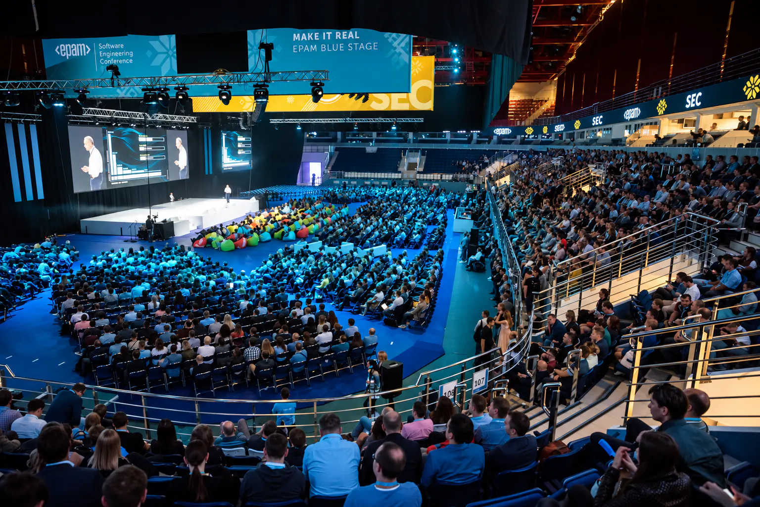 Packed arena and stands facing the EPAM SEC Blue Stage with a speaker on large LED screens