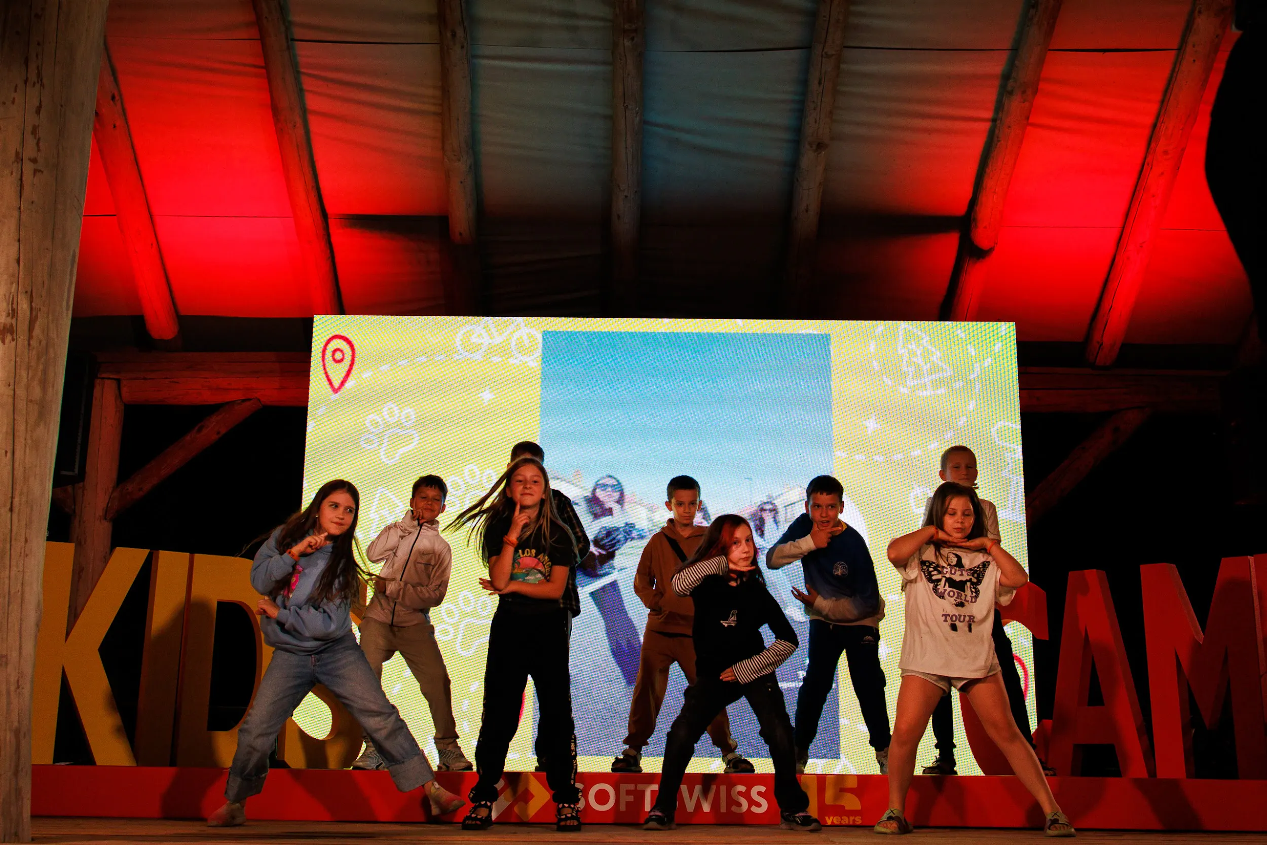 Children performing a dance on the outdoor stage with an LED screen and KIDS CAMP letters