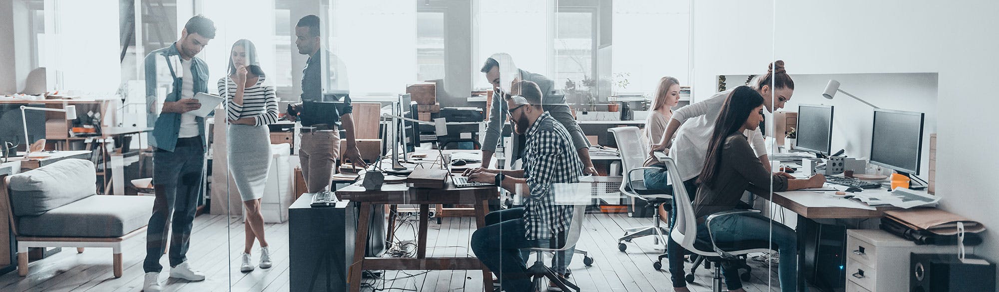 Busy office space with people chatting and working at computers. 