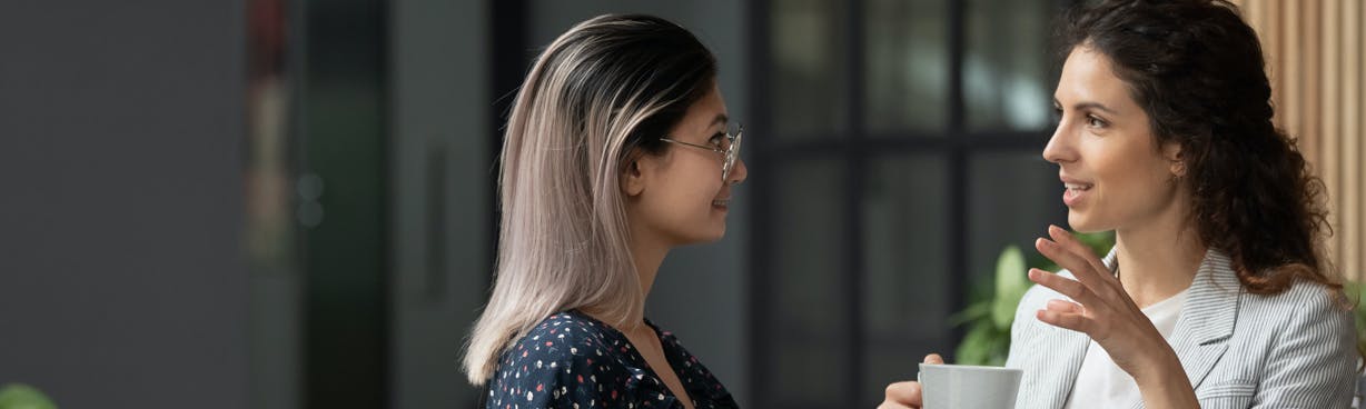 Two women at work, chatting over a coffee.