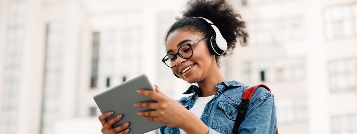 girl wearing headphones and glasses smiling at her ipad