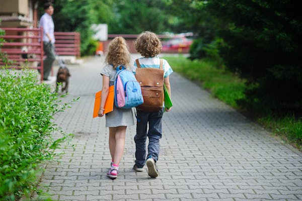 Two children walking along side-by-side with backpacks & school folders