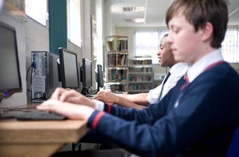 School boys in uniform working on computer stations in school