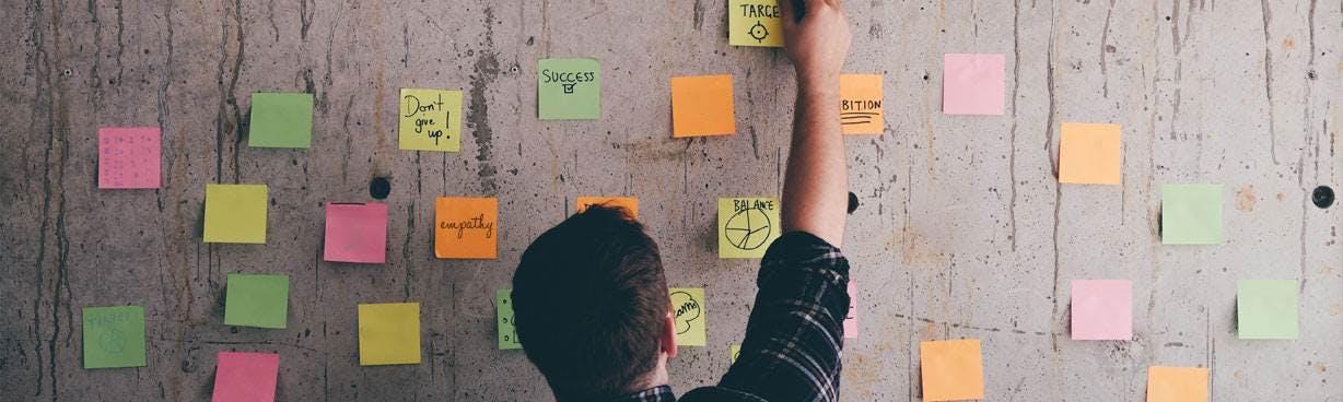 A man putting different colored sticky notes on a wall