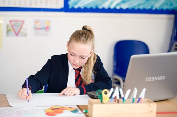 Girl at school using laptop and pen and paper